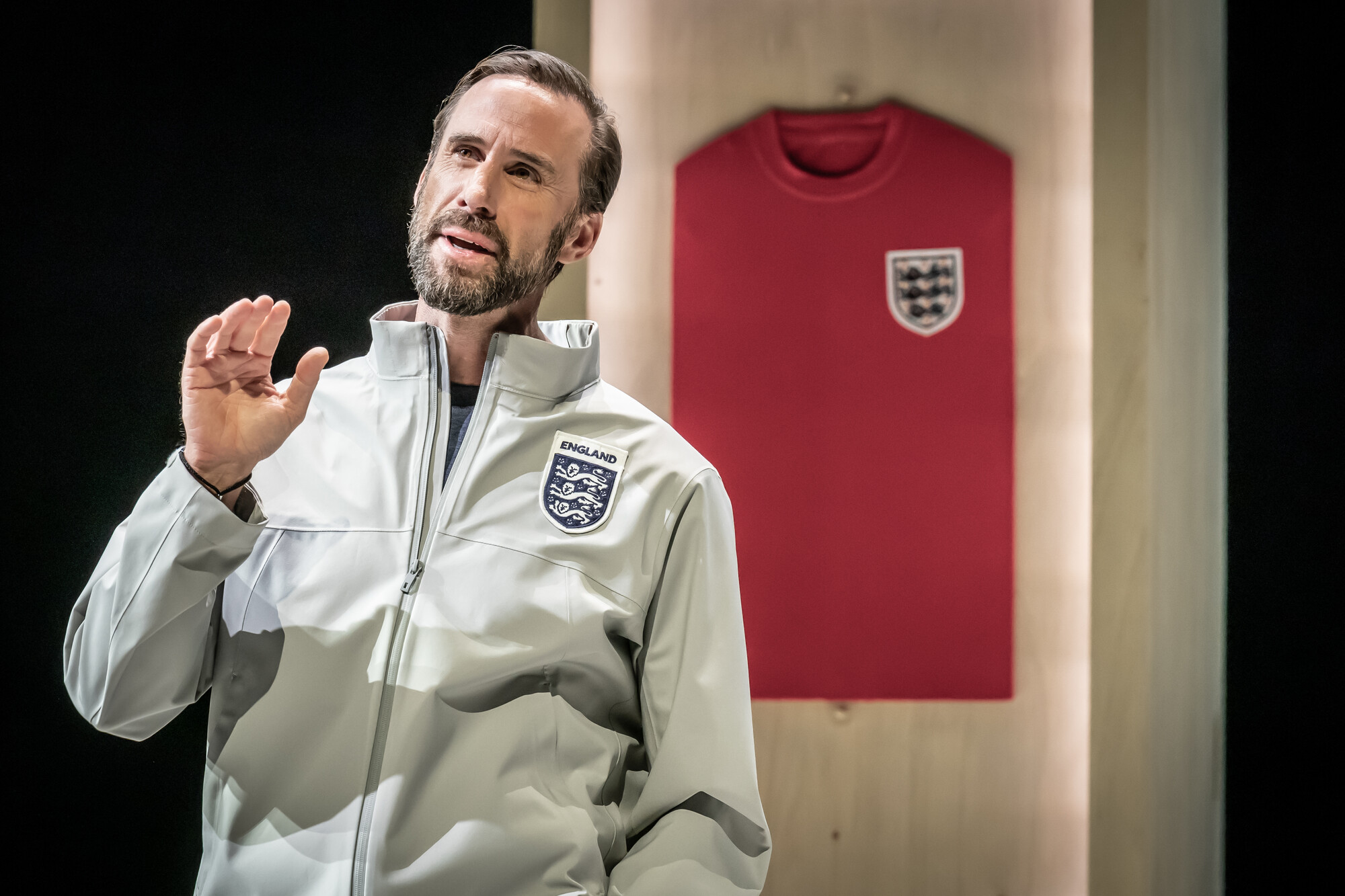 A man in an England football jacket speaks on stage.