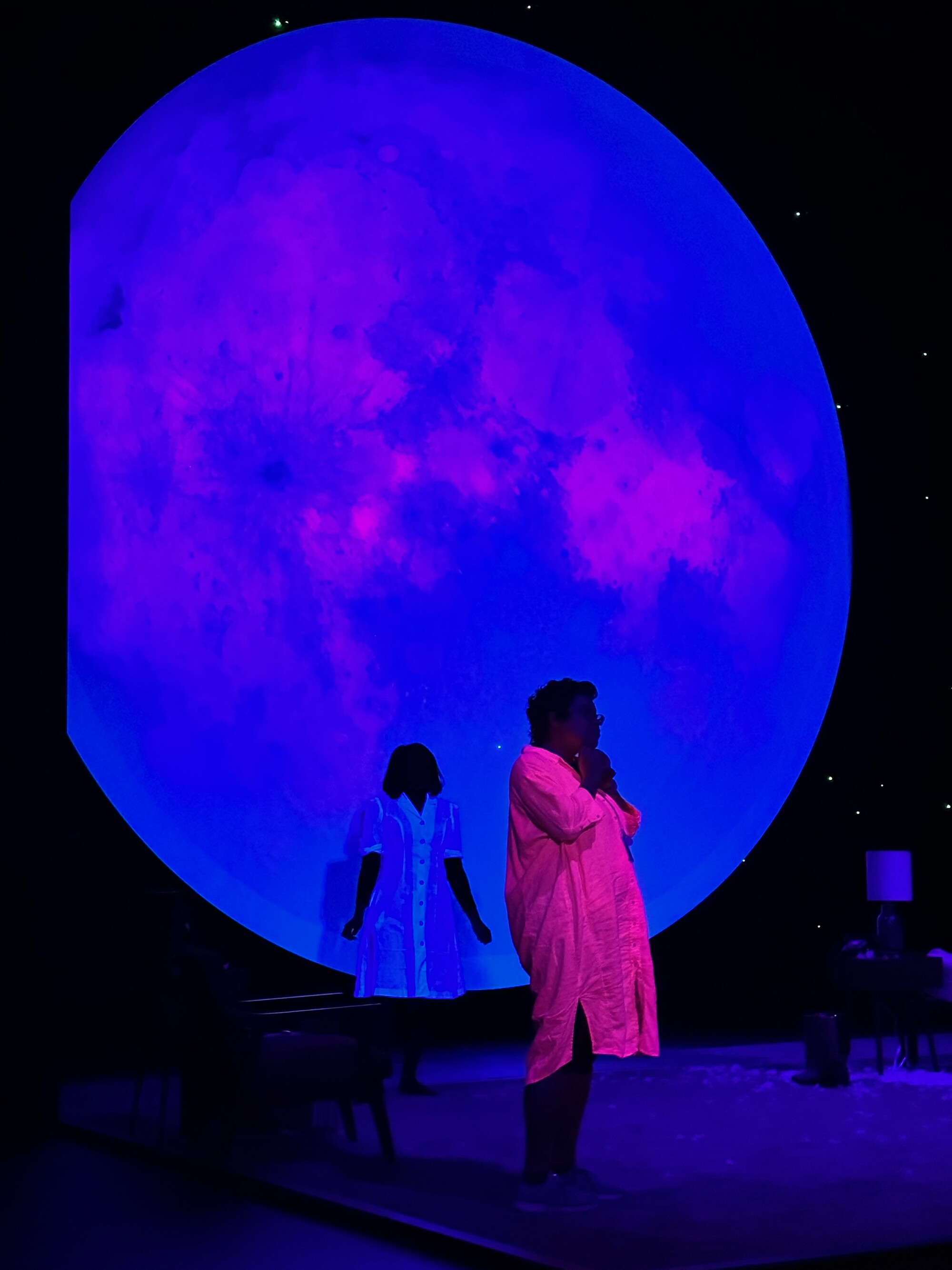 Two people stand onstage in front of a large projection.