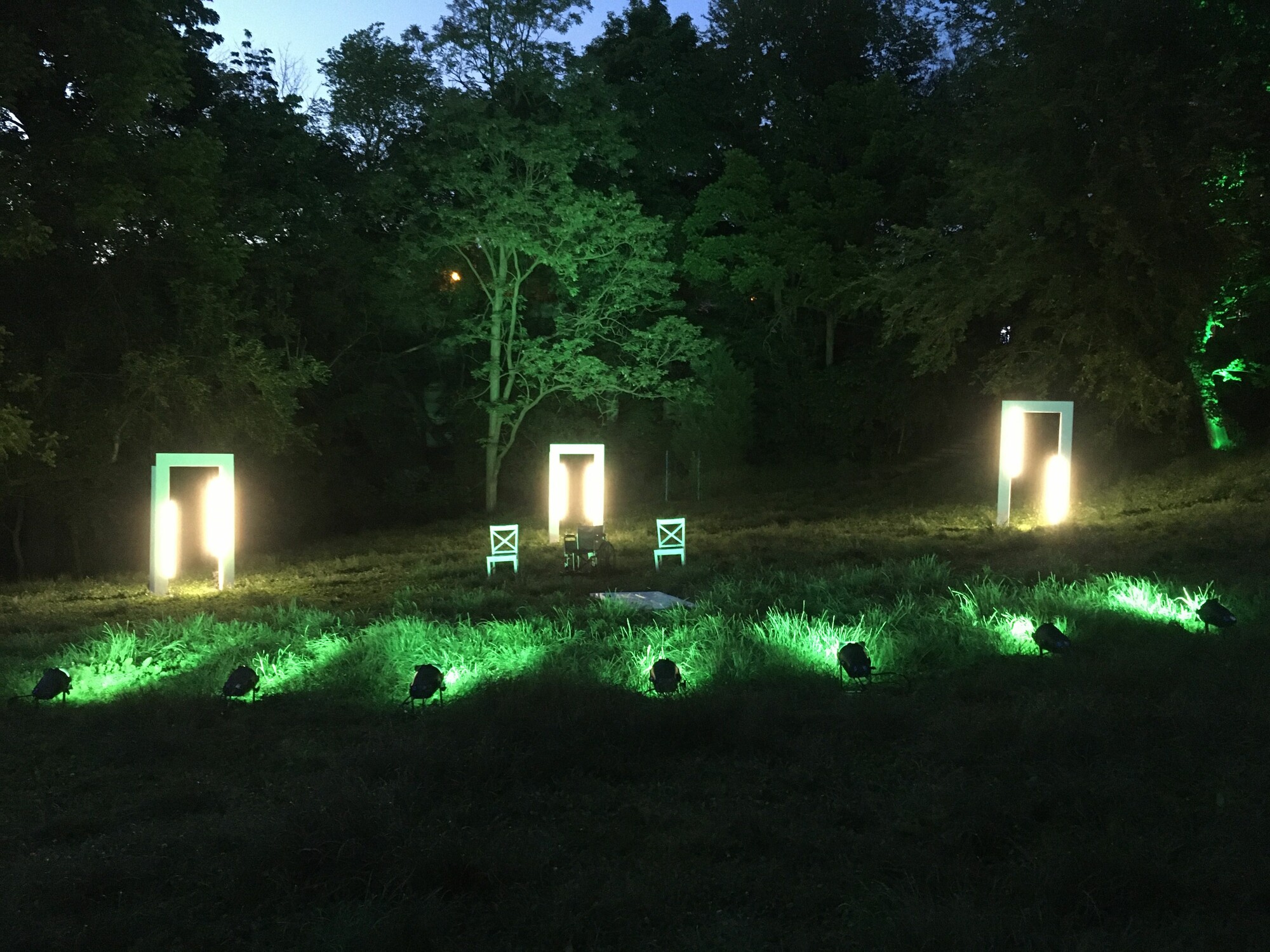 A series of lights illuminate three mirrors at the treeline of a forest.