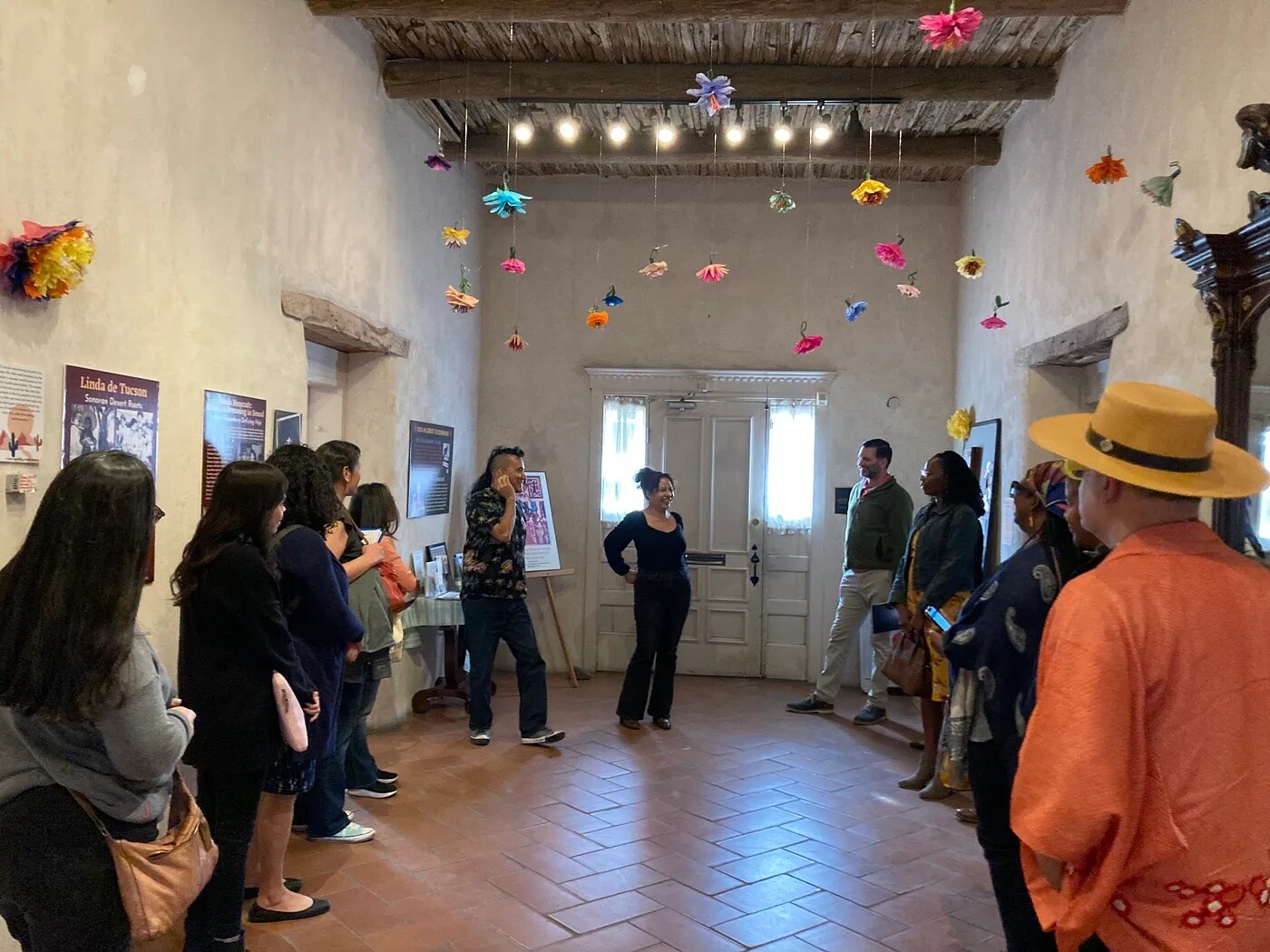A group of people stand in a circle in a small room with colored objects hanging from the ceiling.