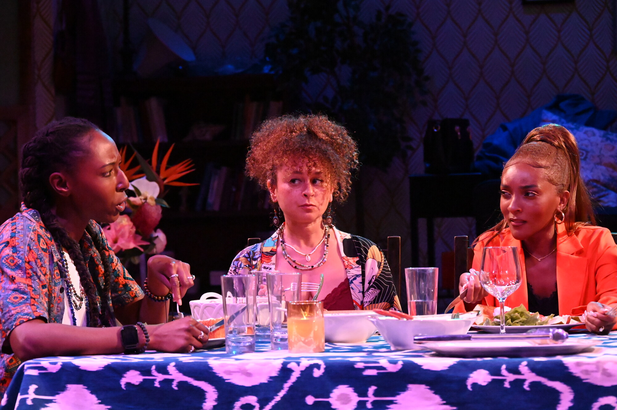 Three actors sit at a table having a conversation.