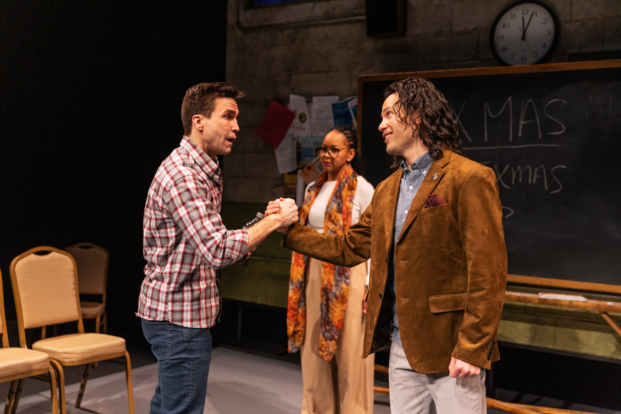 Three actors perform onstage in a classroom set.