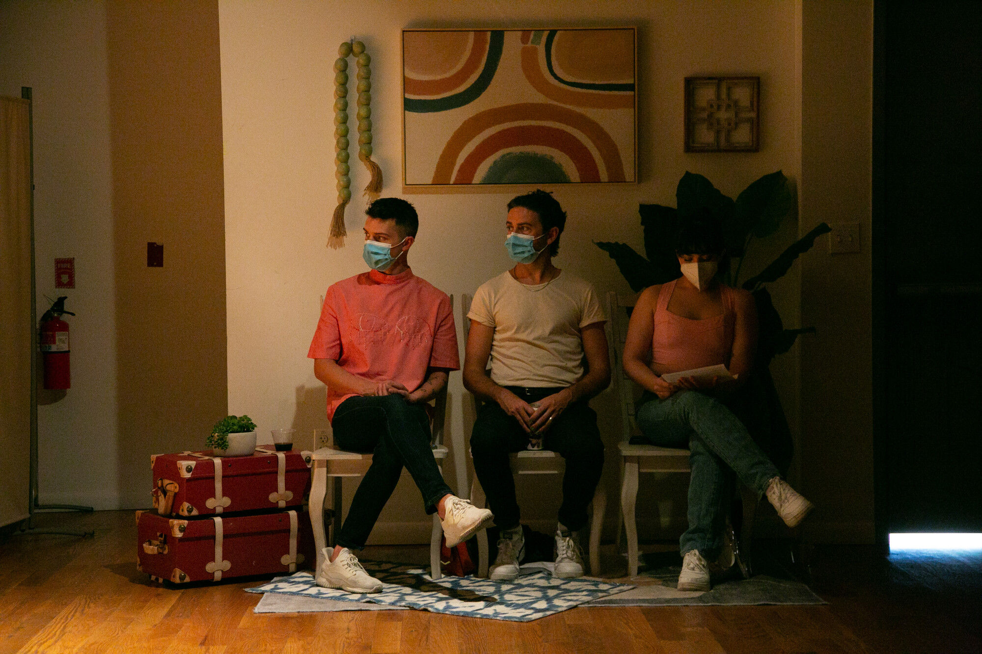 Three audience members in masks sit in a decorated room.