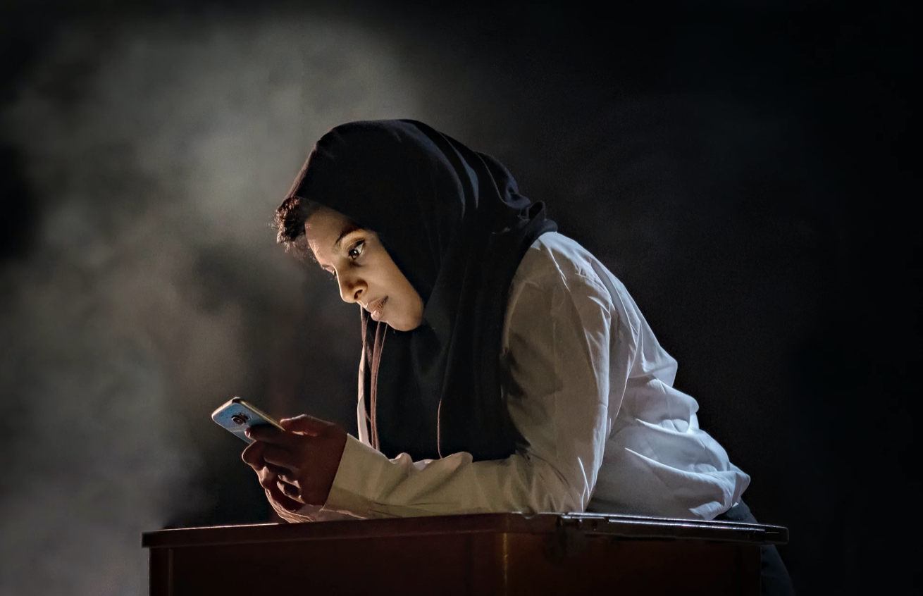 A woman in a hijab leans over a cell phone onstage.