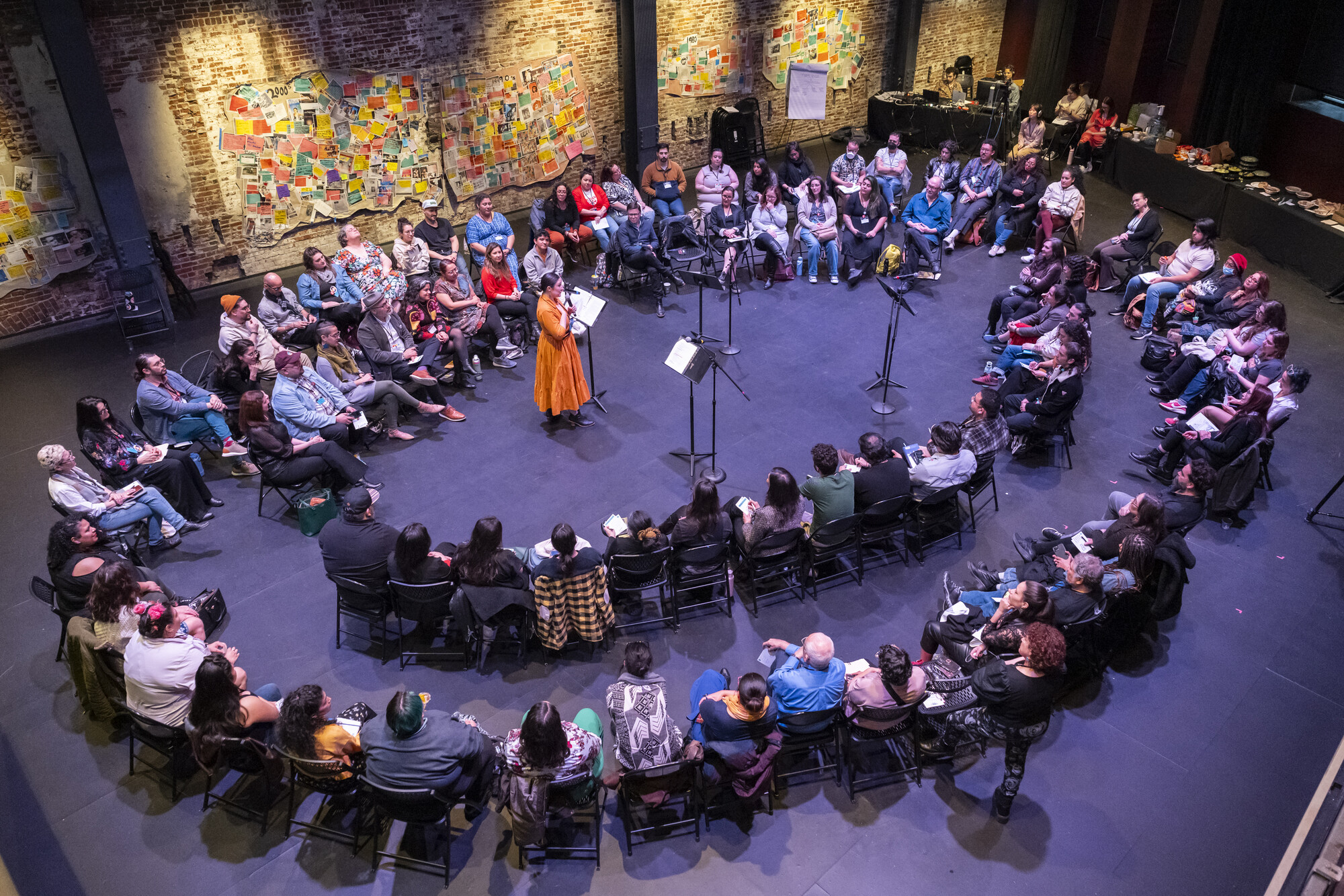 A group of people sit in chairs in a circle listening to a speaker.