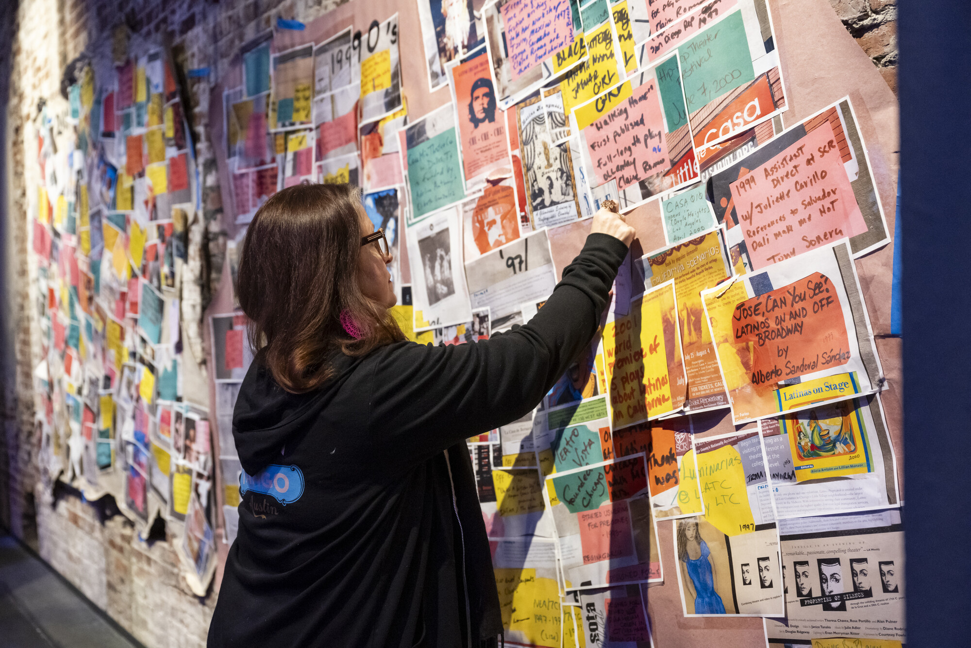 A woman examines a collaged wall of papers.