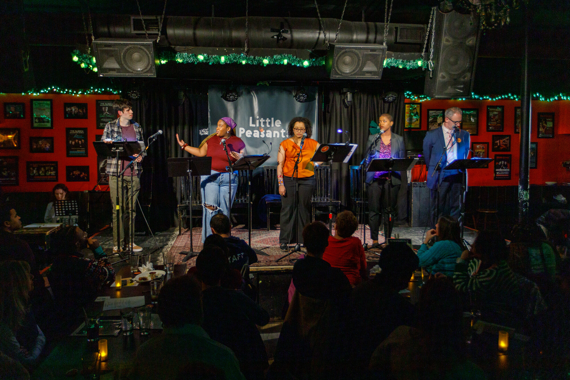  A group of people stand on stage reading from music stands.