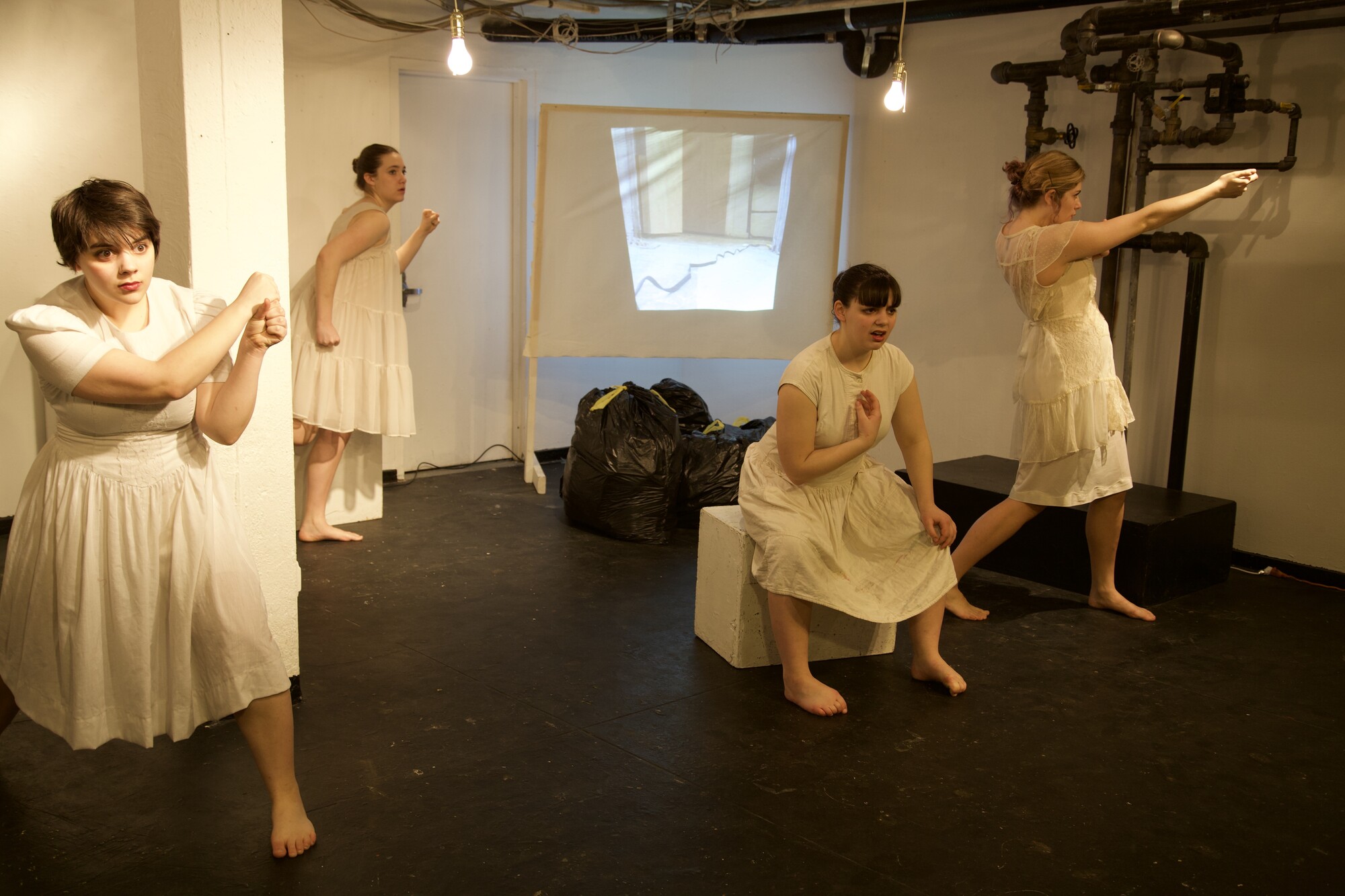 Four dancers dressed in white dance in front of a brightly lit white background.
