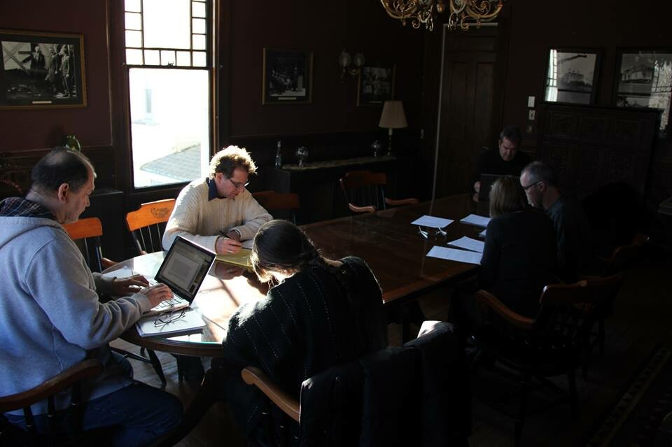 Writers work at a table on laptops in a dimly lit room.