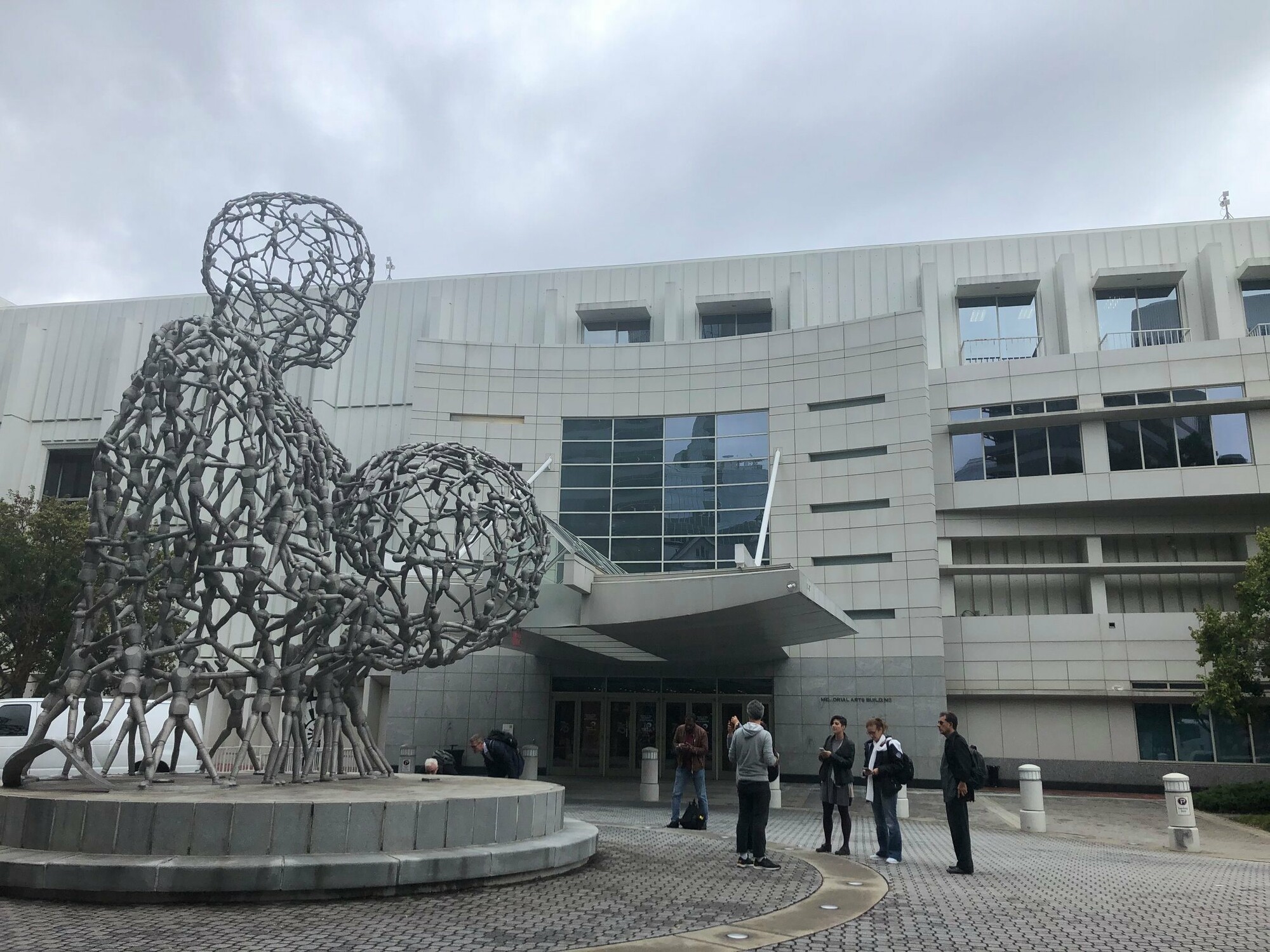 A group of people stand outside of the Alliance Theatre in front of a large wire sculpture.