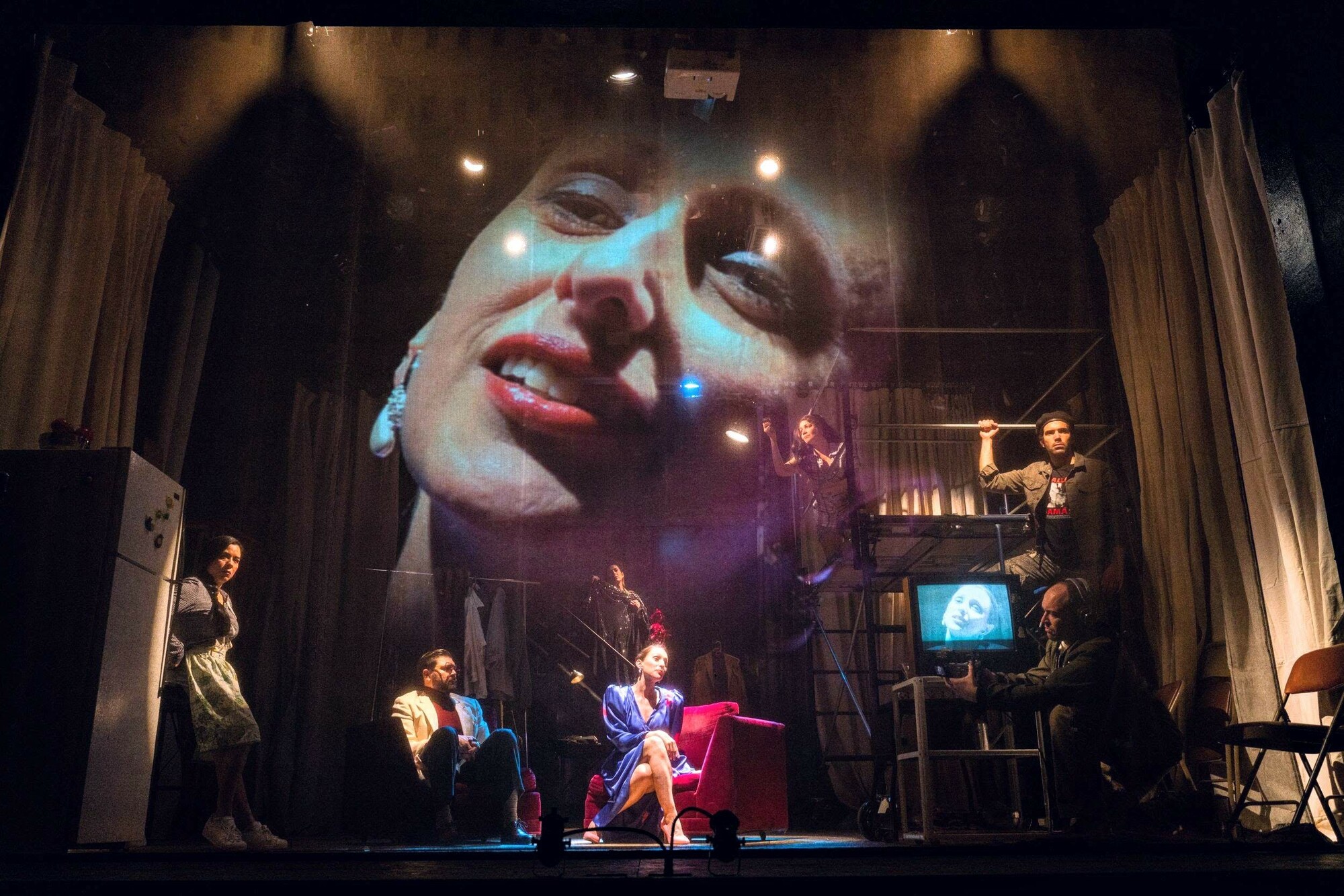 A woman sings on a crowded stage in front of a live projection of herself.