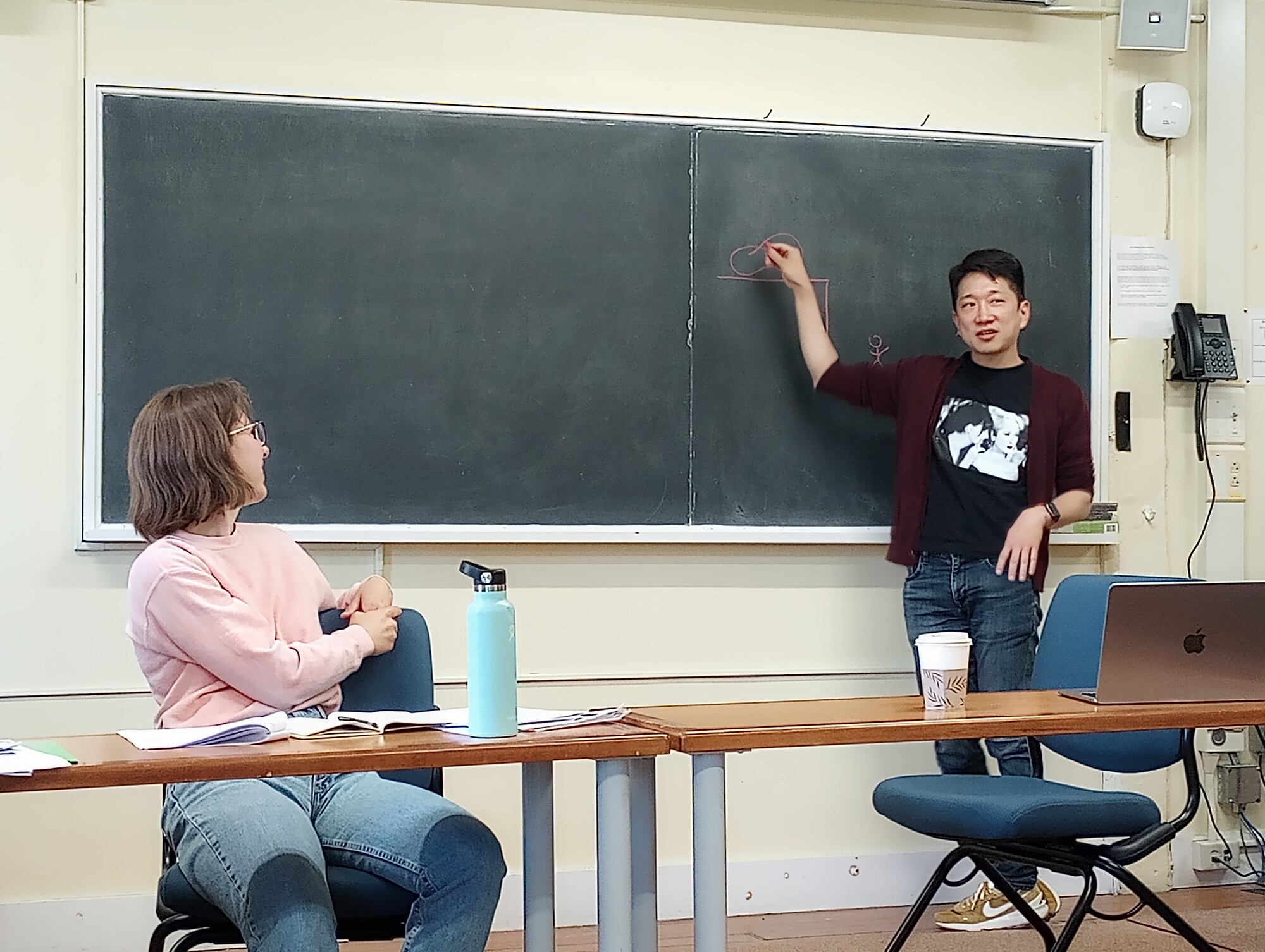 An artist stands in front of a chalk board in a classroom.