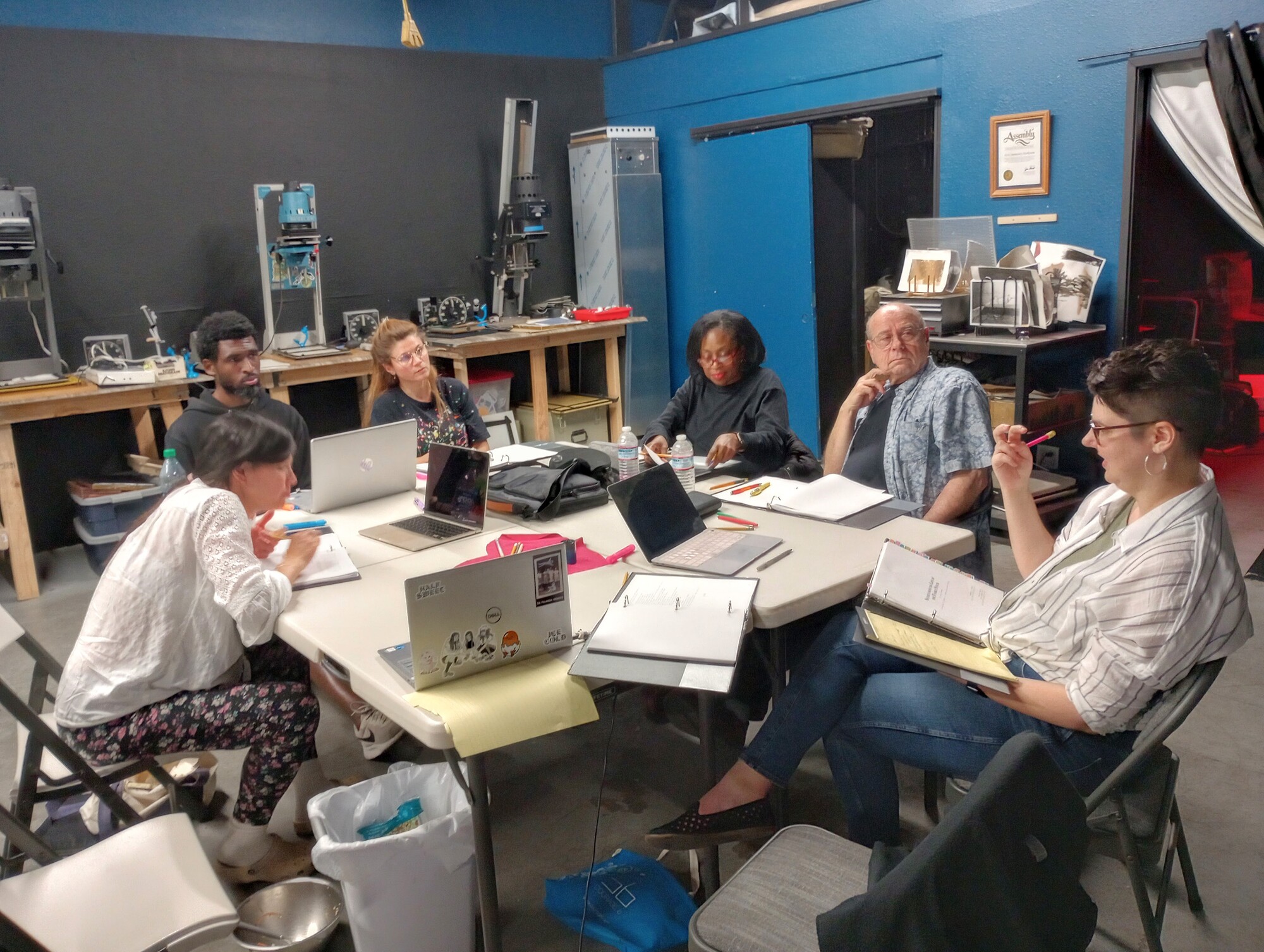 A group of artists work around a table with laptops and scripts in front of them.