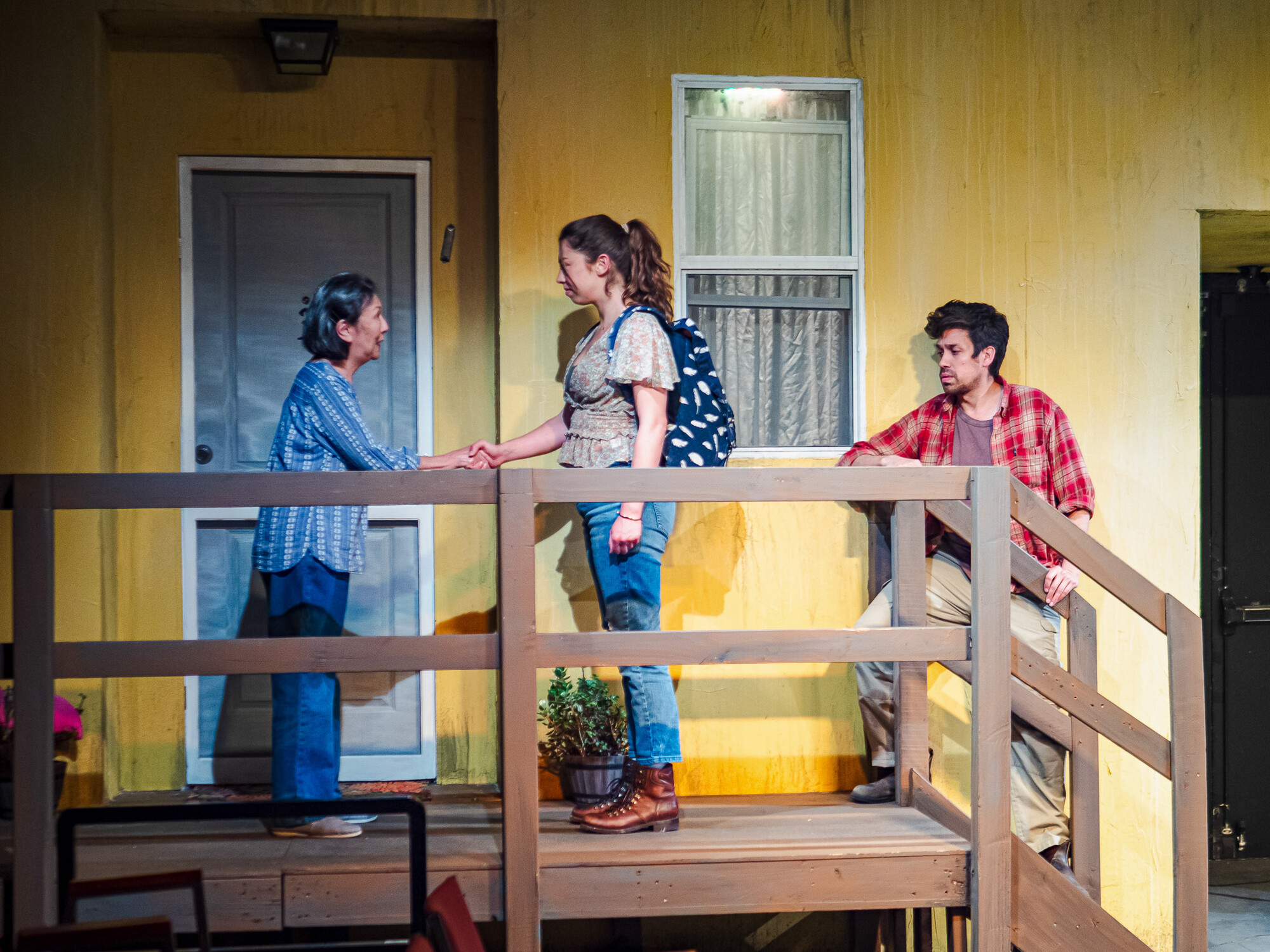 The actors stand on a porch on a brightly lit stage.