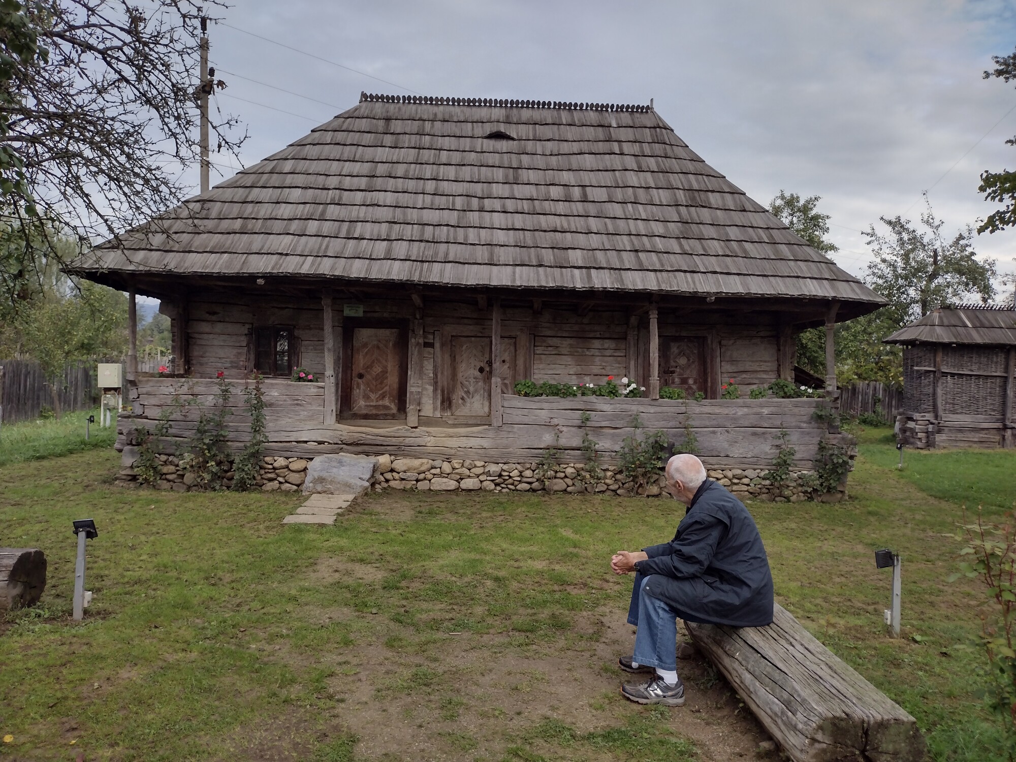 A person sits on a bench in front of an old cottage on a cloudy day.