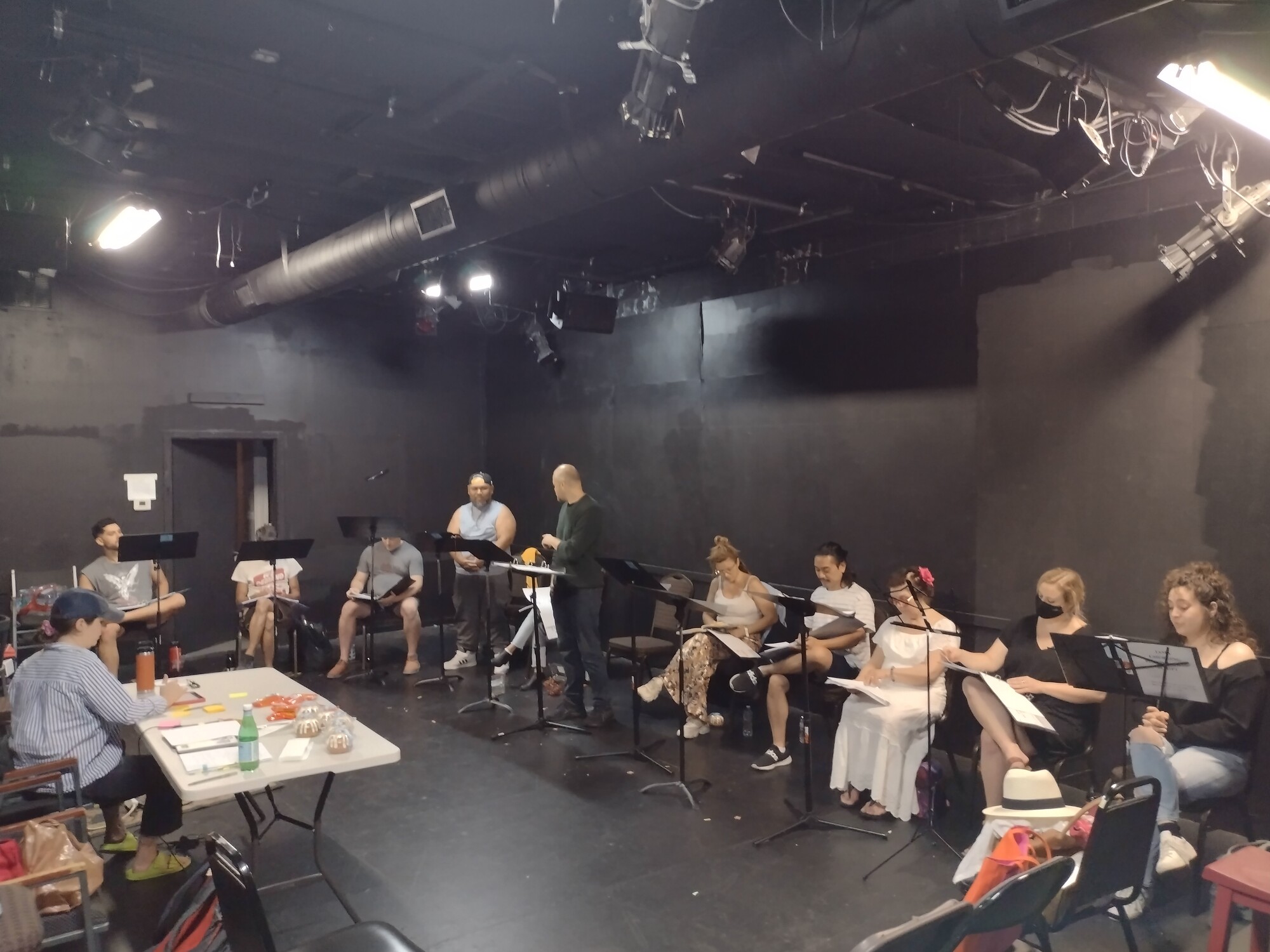 A group of people participate in a reading in a black box theatre.