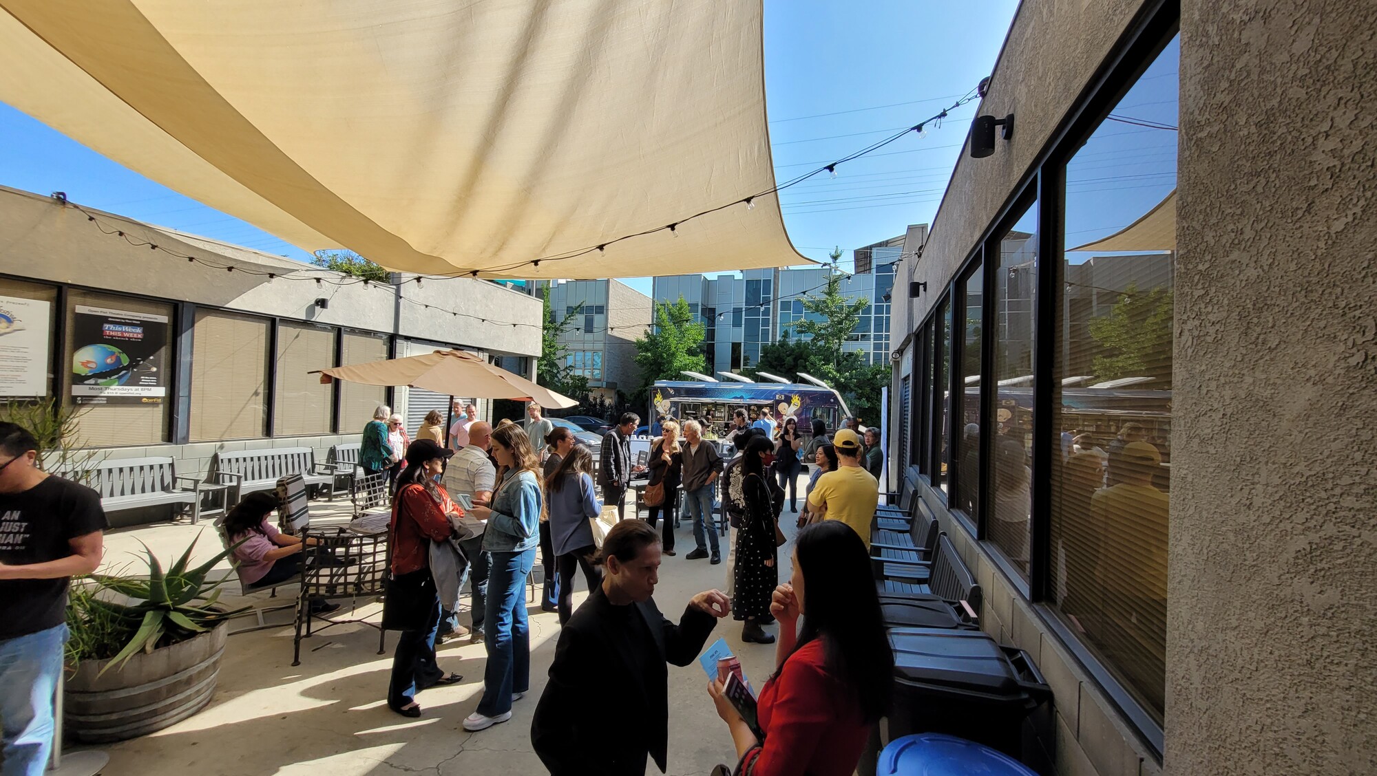 A group of people mingle outside of a theater on a sunny day.