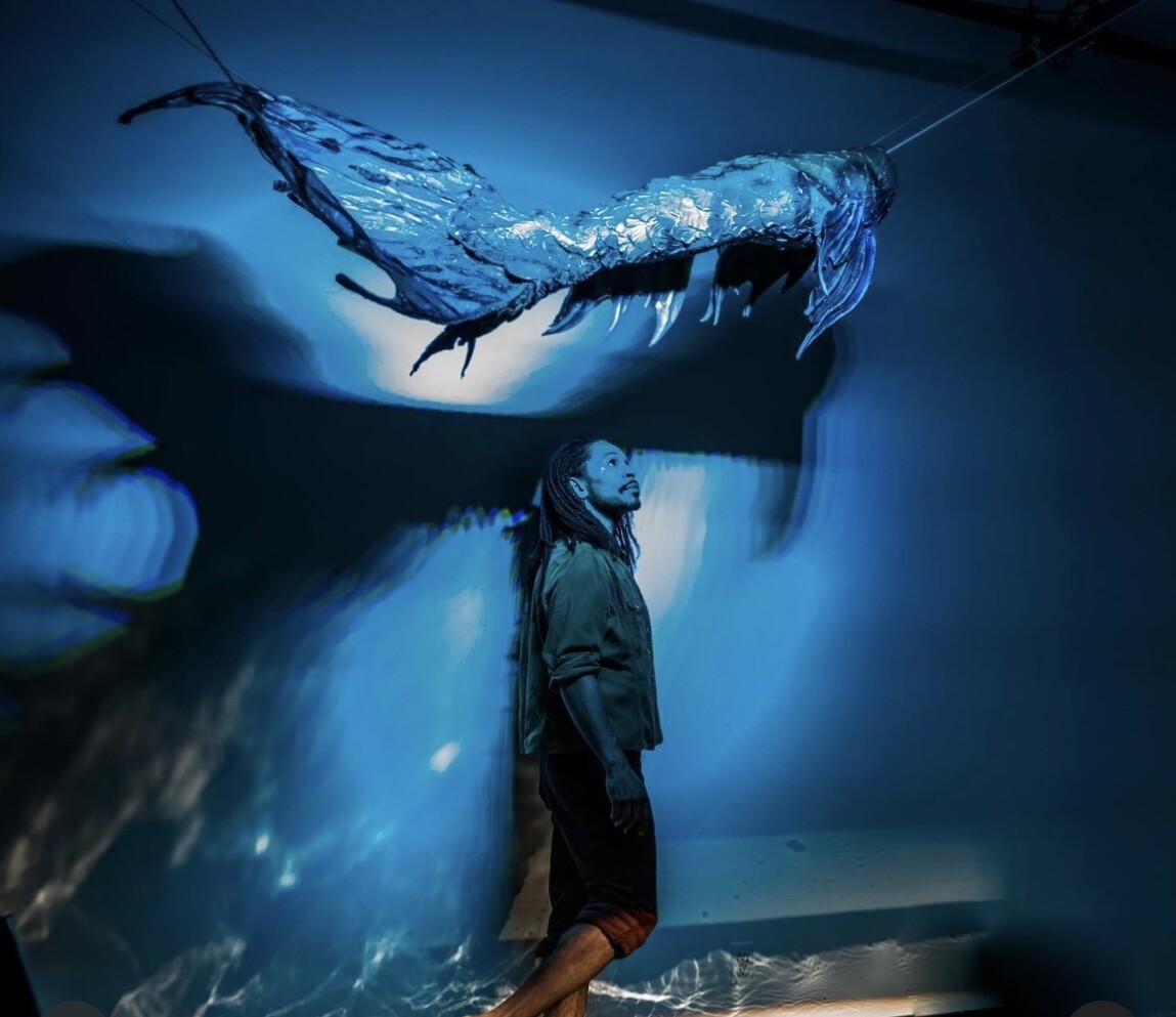 A person in blue lighting looks up at a sculpture. 