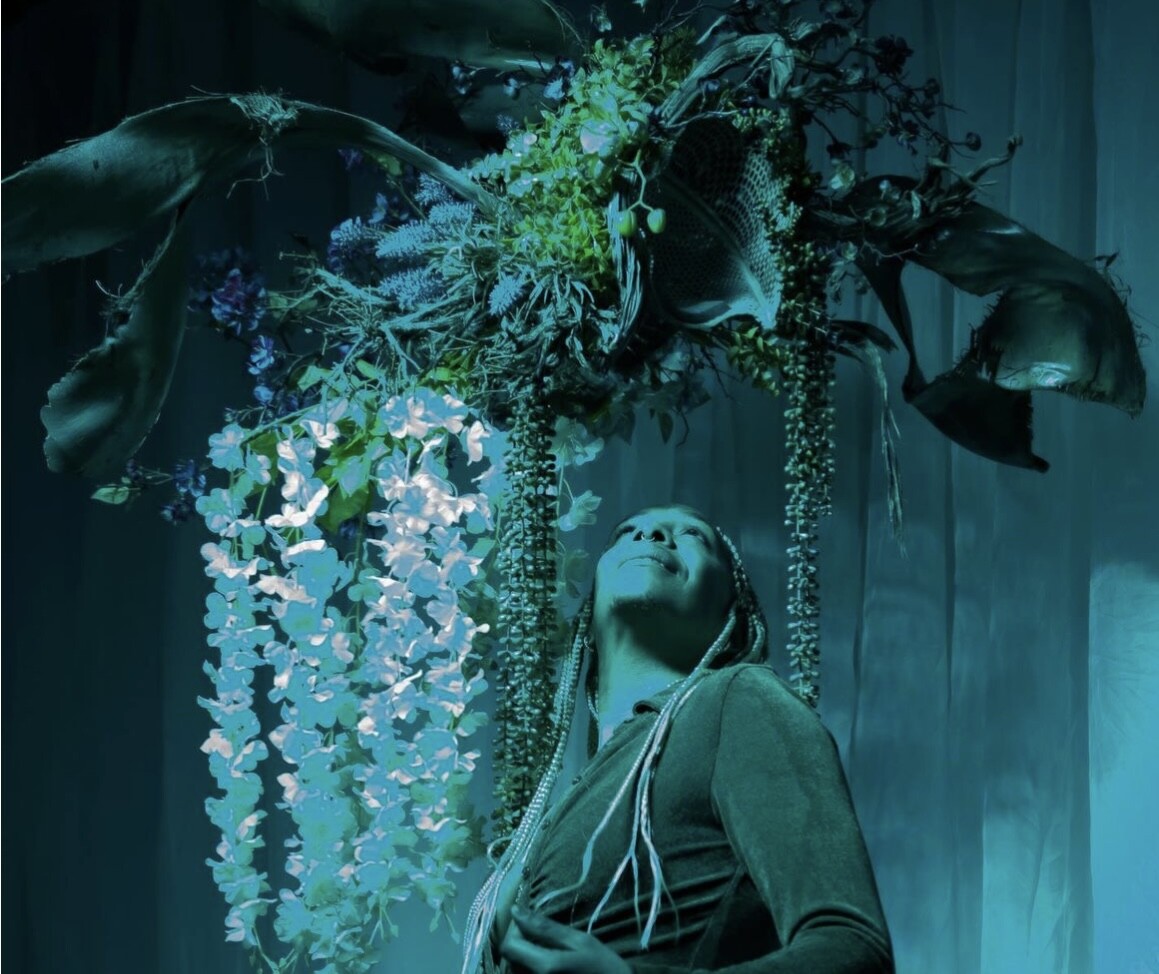 A person in green lighting looking up at a floral sculpture.