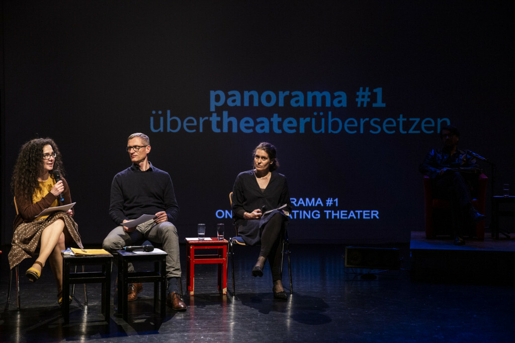 Three people sit onstage with microphones speaking on a panel.