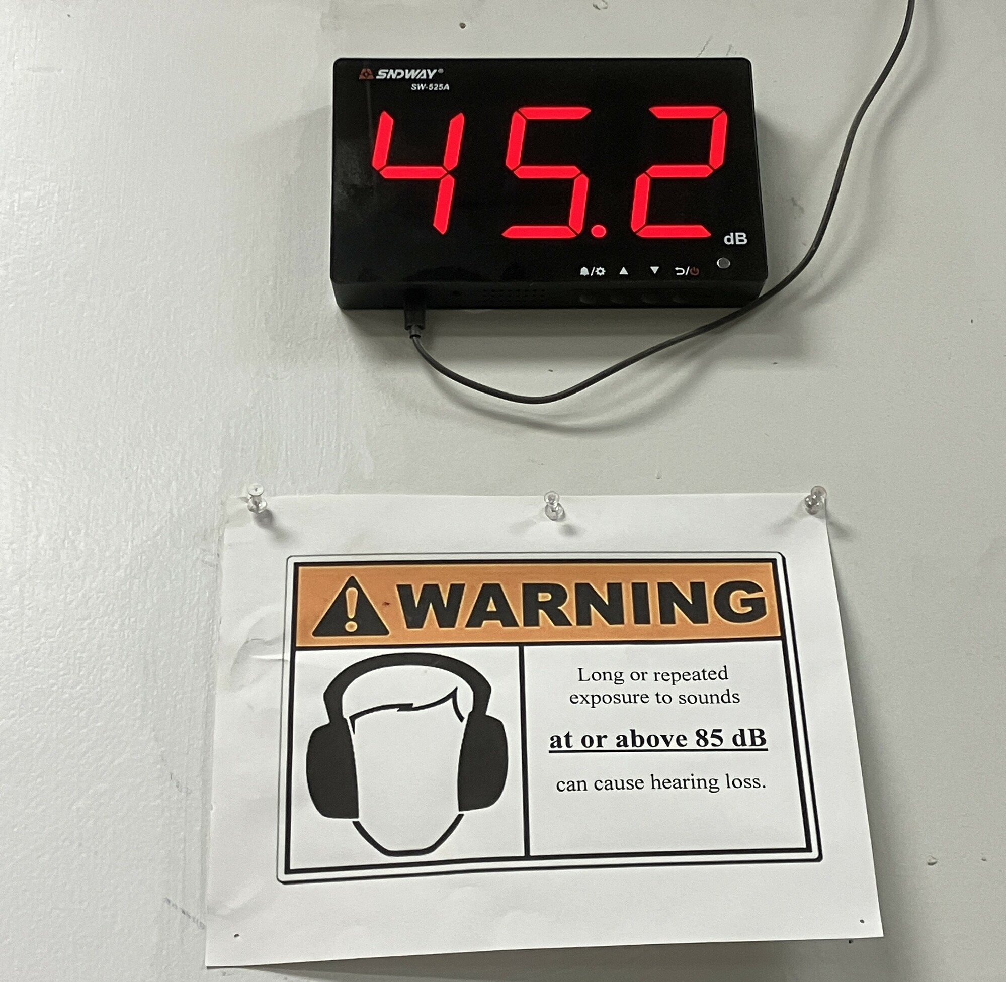 A decibel meter that reads 45.2 and a sign warning about high decibel sounds. 