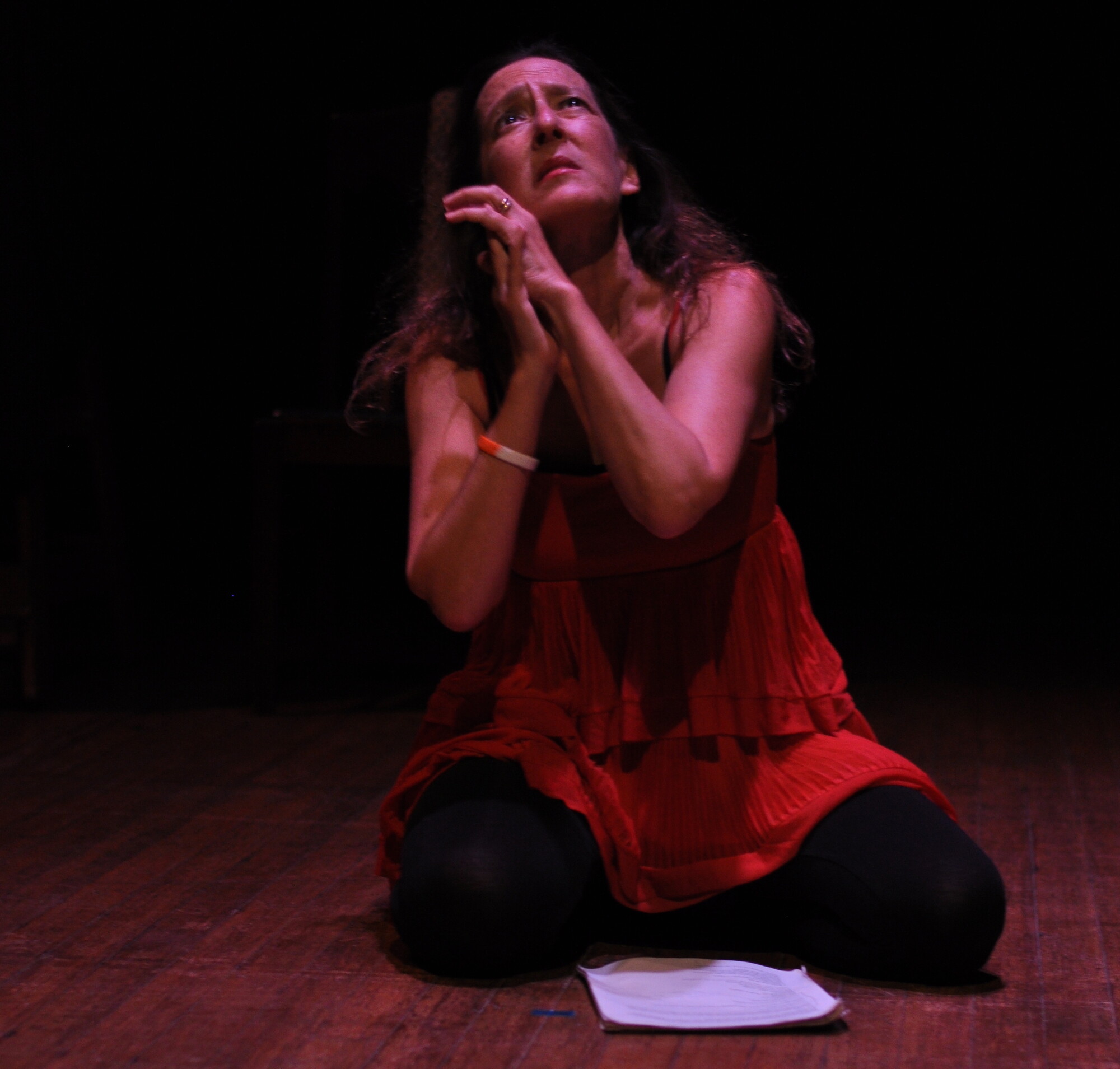 A woman kneels on the floor in a red dress.