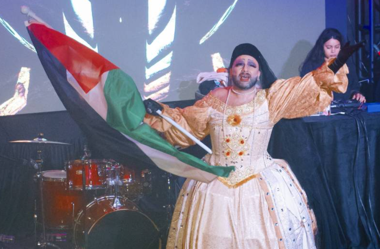 A person in drag waving a Palestinian flag on stage. 