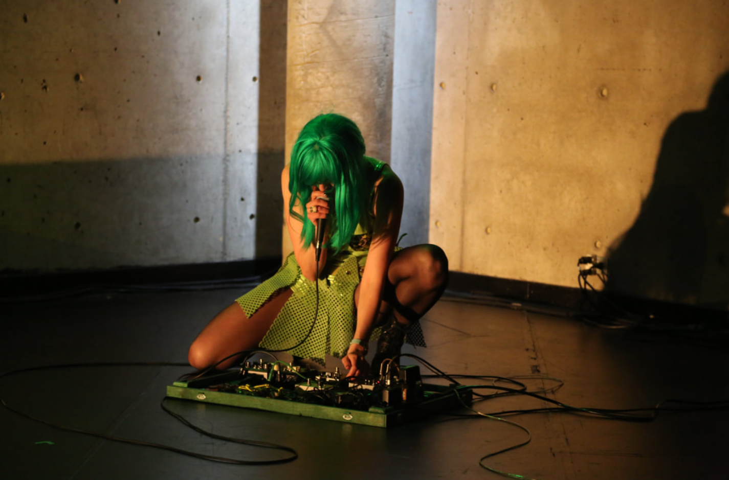 A person in a green wig uses a sound board on stage. 