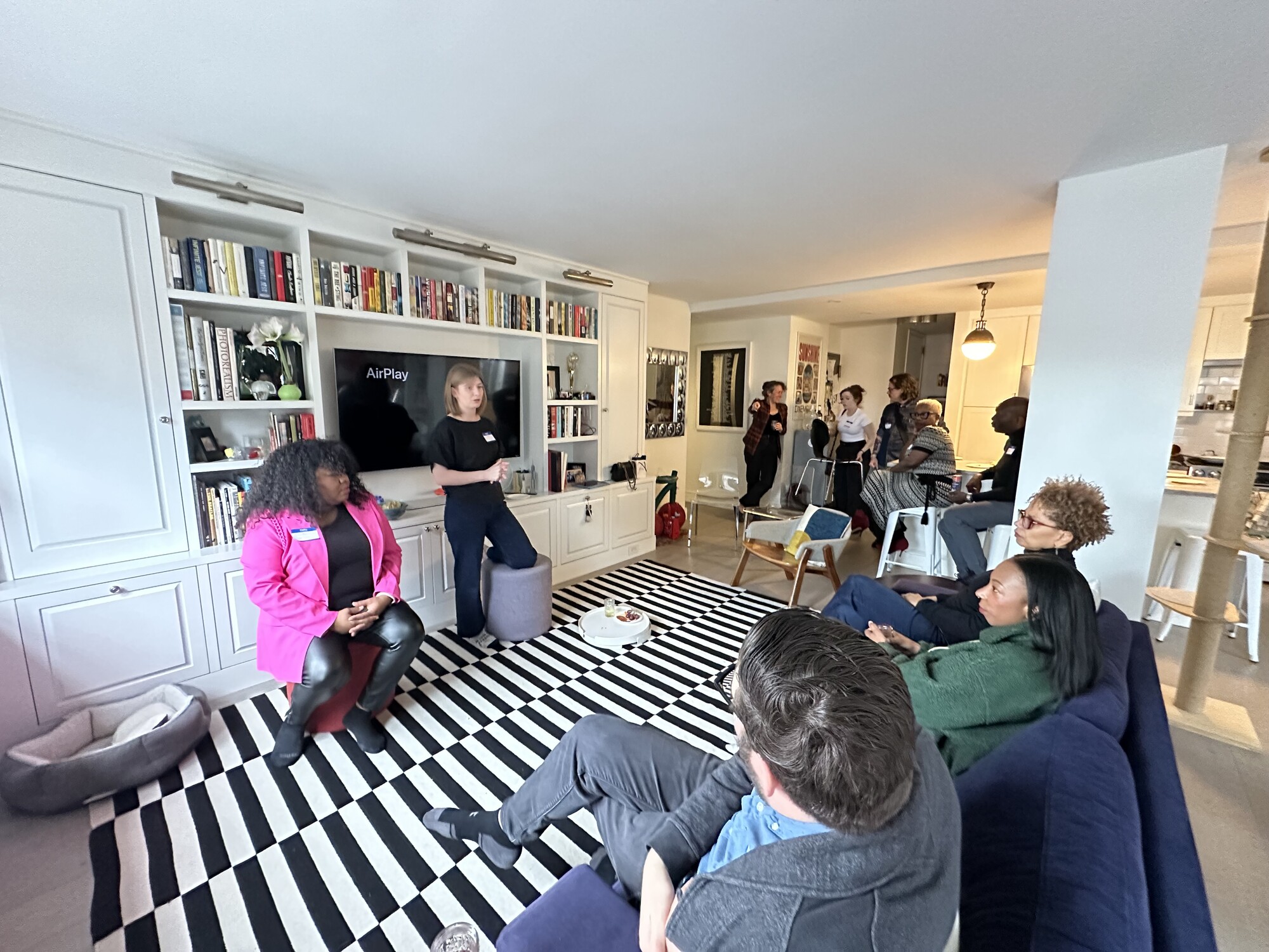 A group of theatre makers sit in a circle in a brightly lit room filled with rugs and bookshelves.