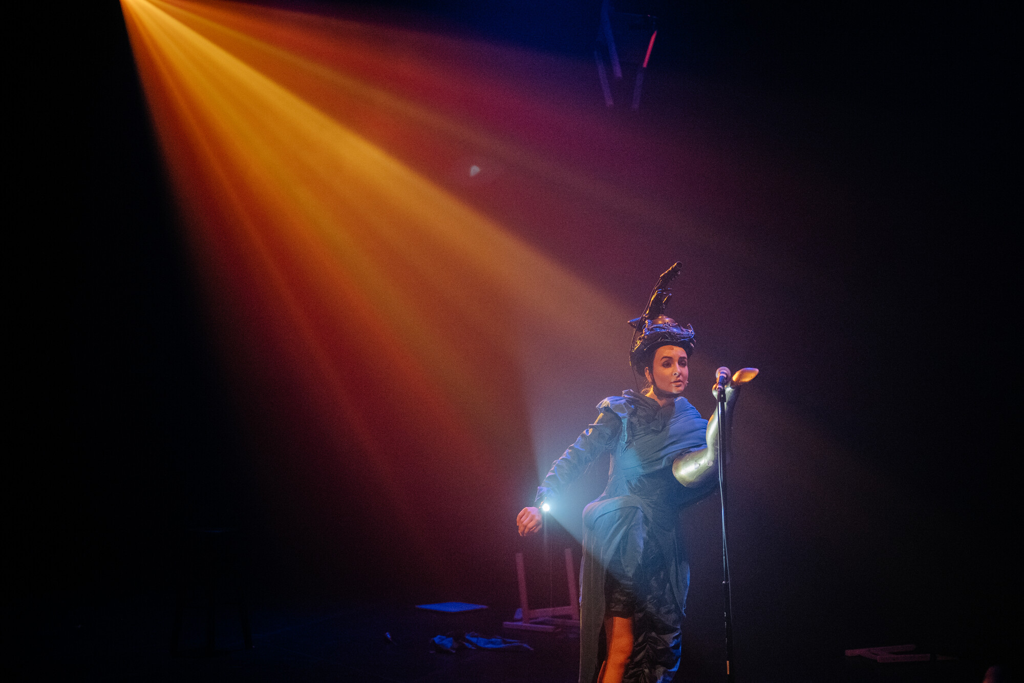 An actor wearing a helmet performs onstage, under a warmly lit spotlight