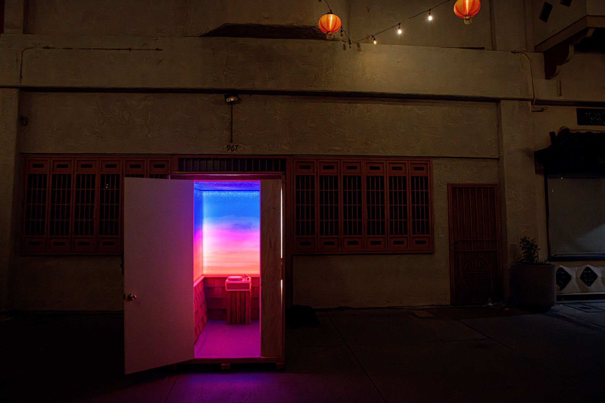 A dimly lit room with a door opening to a smaller room with bright pink light. 