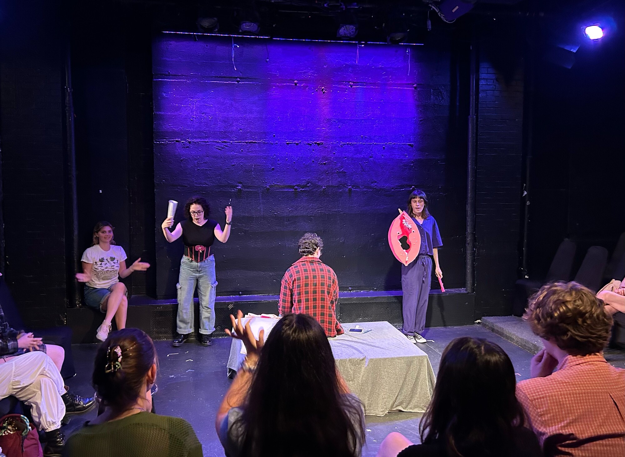 Four people stand on a stage with various props. 