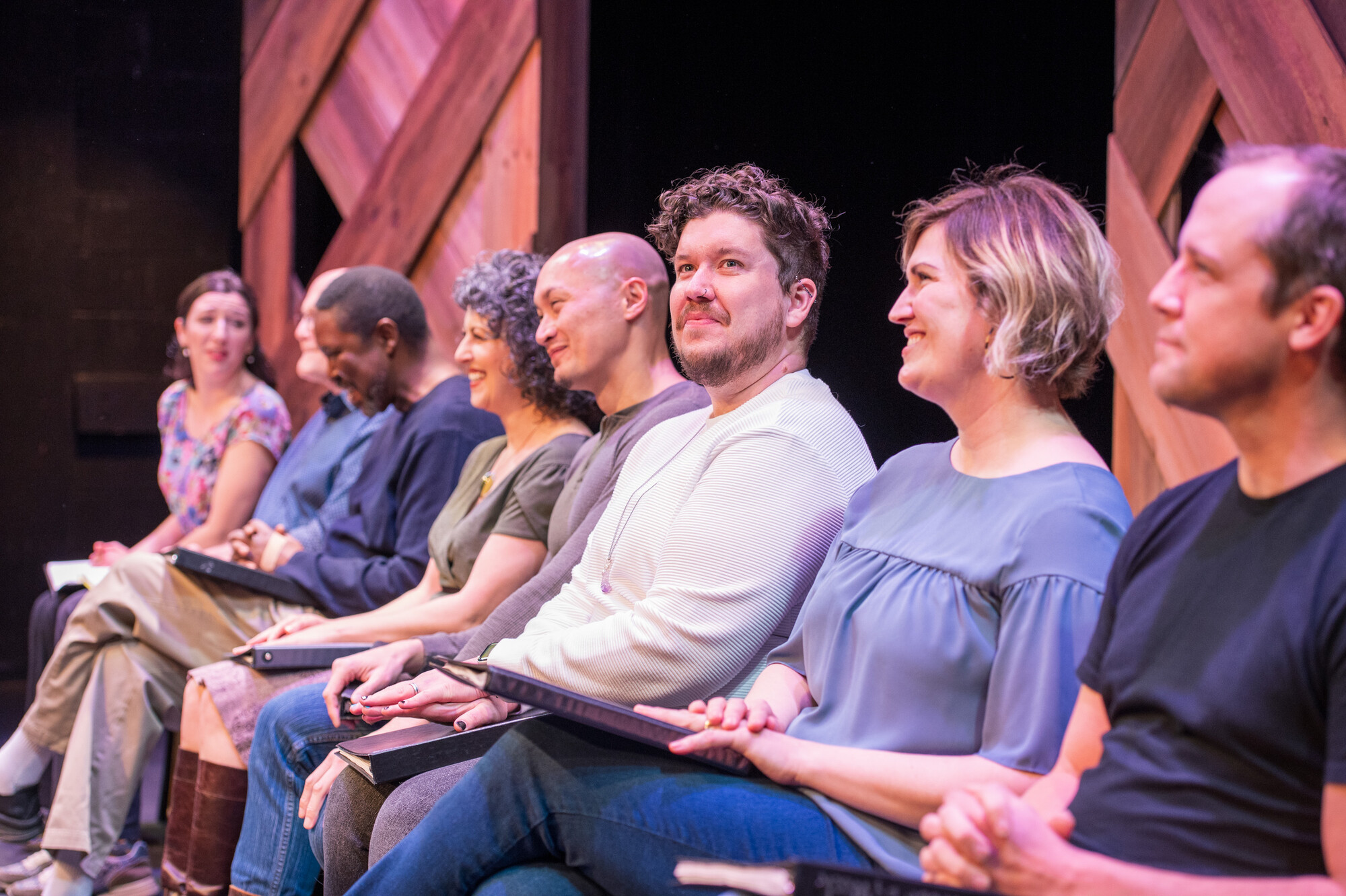 A group of people sit in a line on stage. 