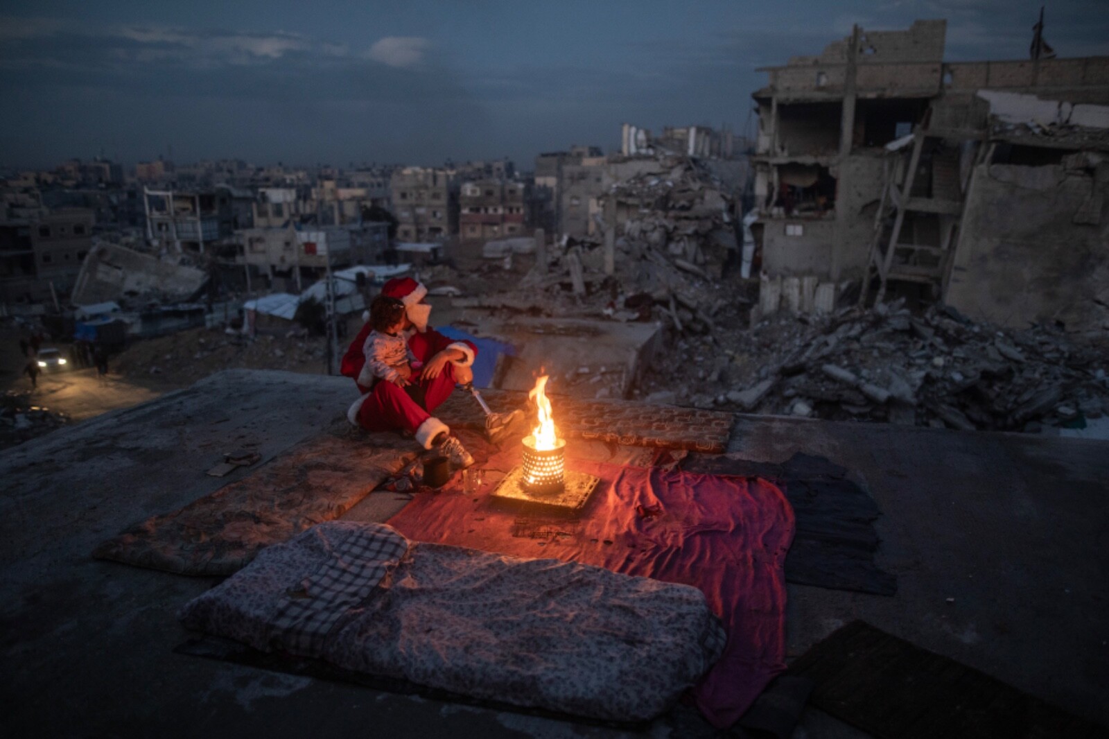 A man dressed up as Santa sits by a fire with a child in Palestine.