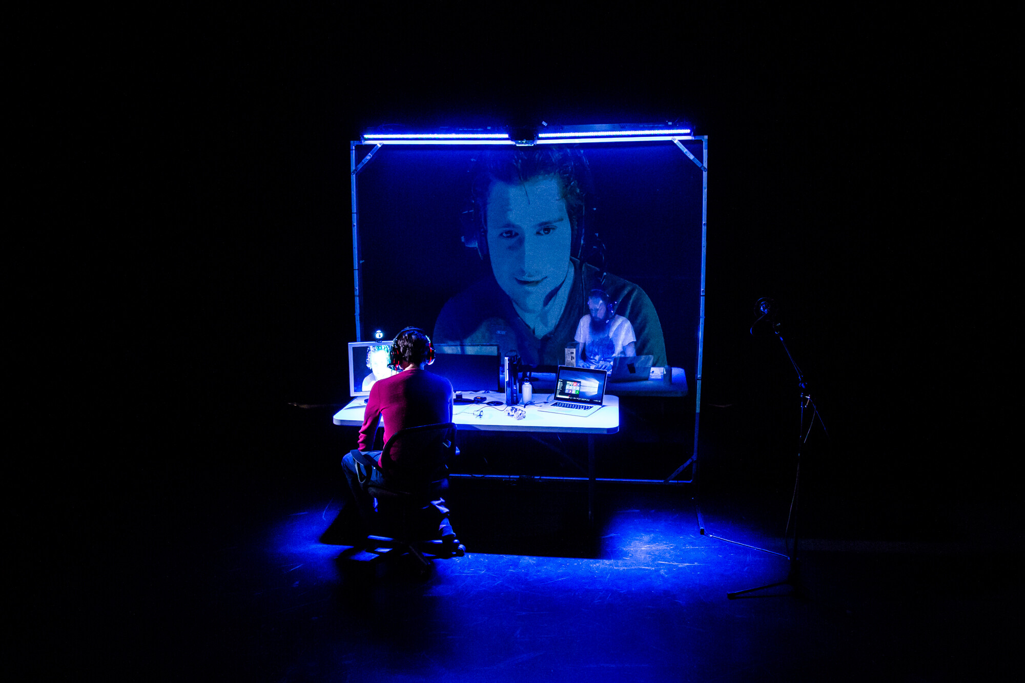 A man using computers and displaying his face on a large screen. 
