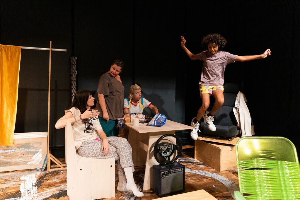 A group of people on stage gather around a table and one person jumps in the air. 