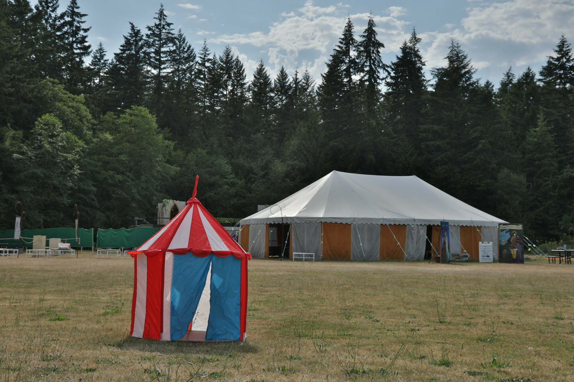 A large field with a small red and white striped tent in the foreground and a large white event tent in the background.