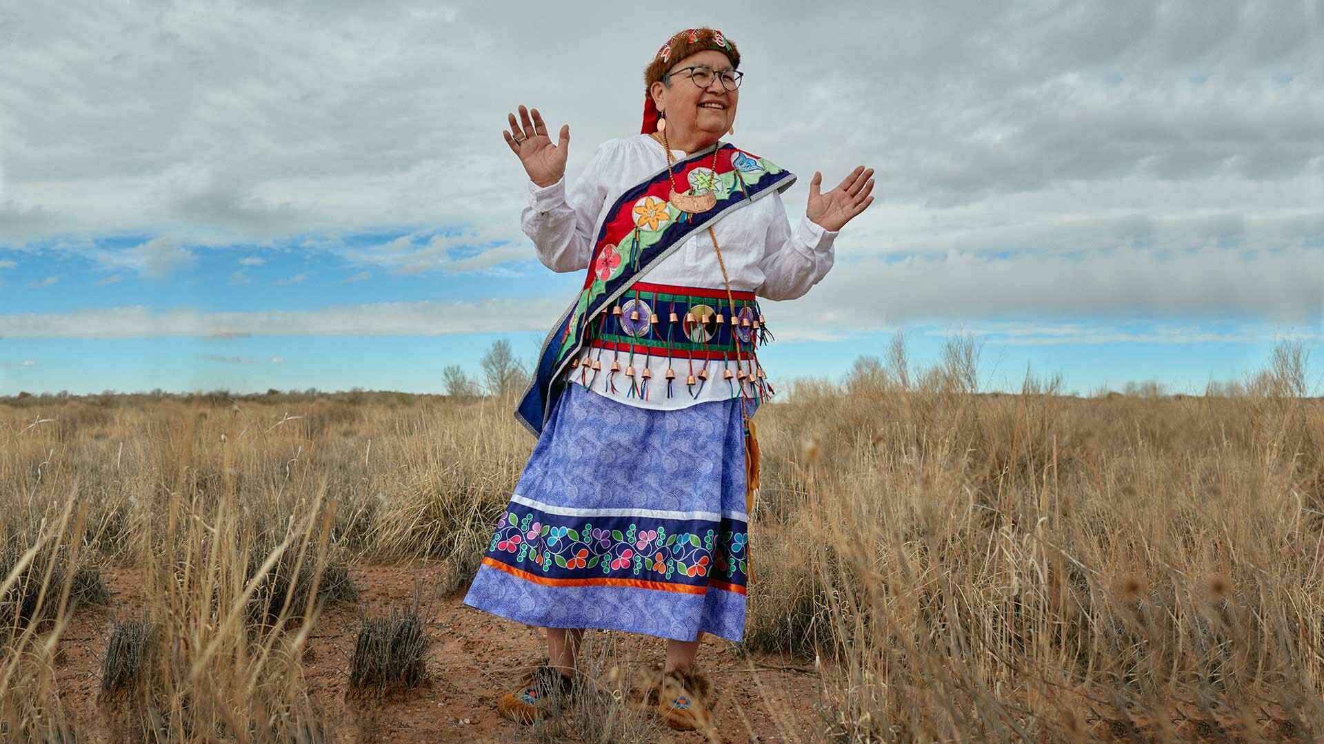 A woman standing in a field wearing a color full skirt and dress.