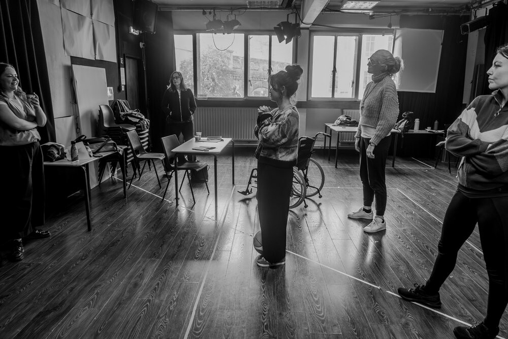 A few people standing in a rehearsal space. 