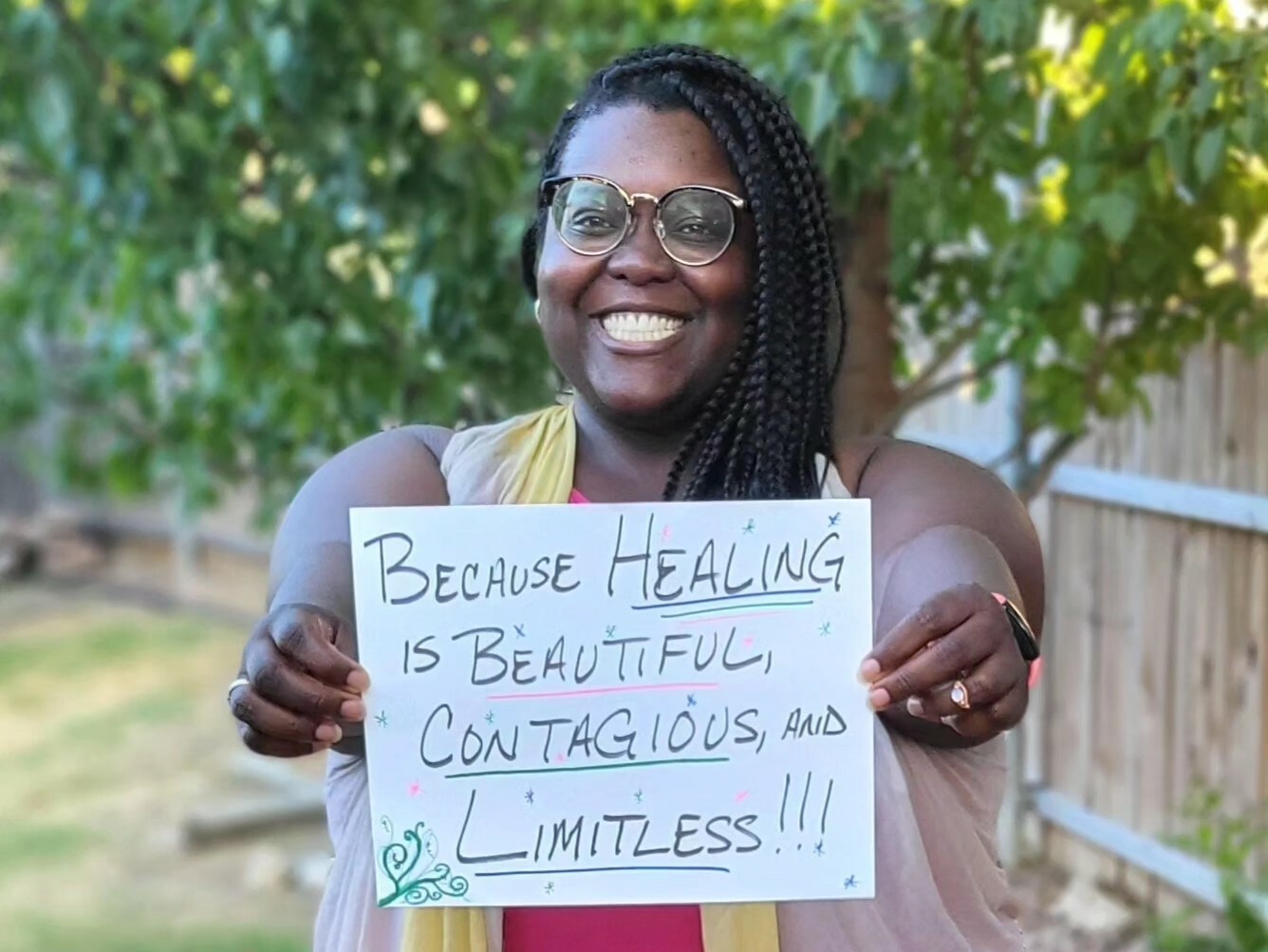 A black woman holding a sign that reads "because healing is beautiful, contagious, and limitless."