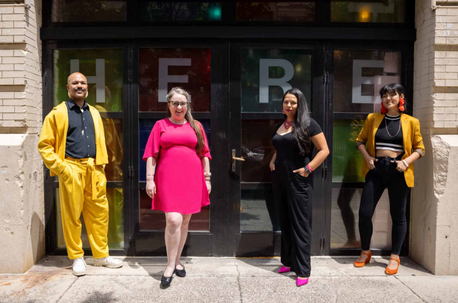 Four people stand in front of a door that says "here."