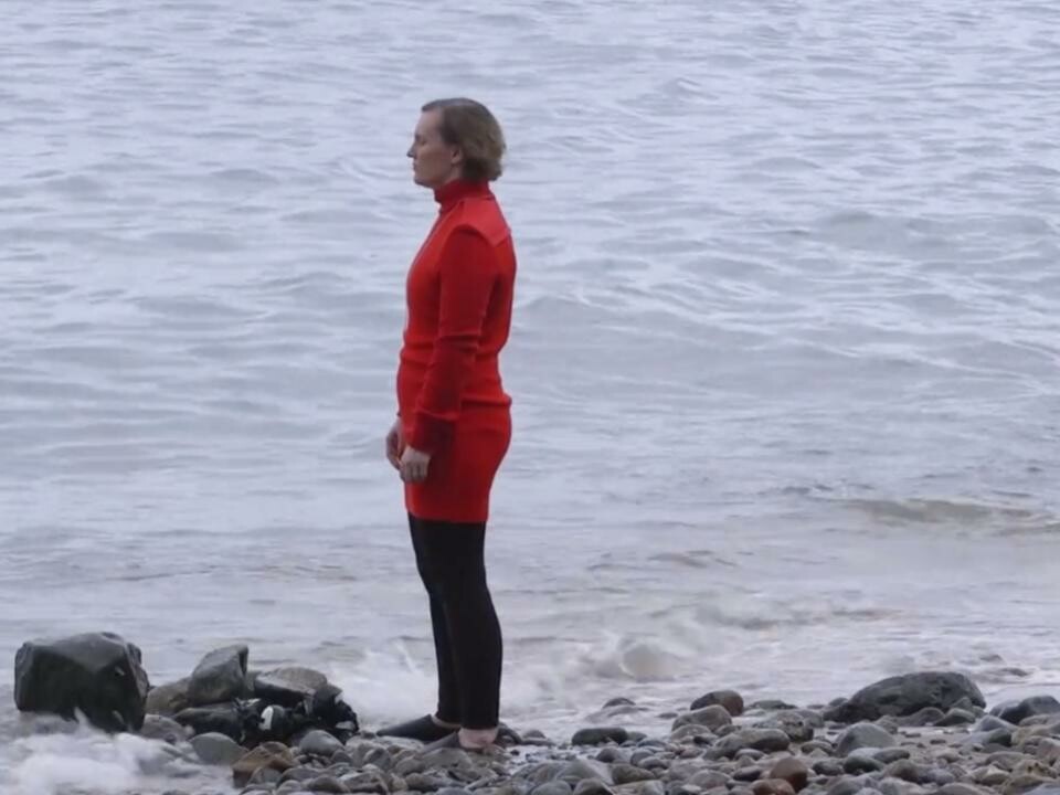 A person dressed in red stands on rocks near a body of water. 