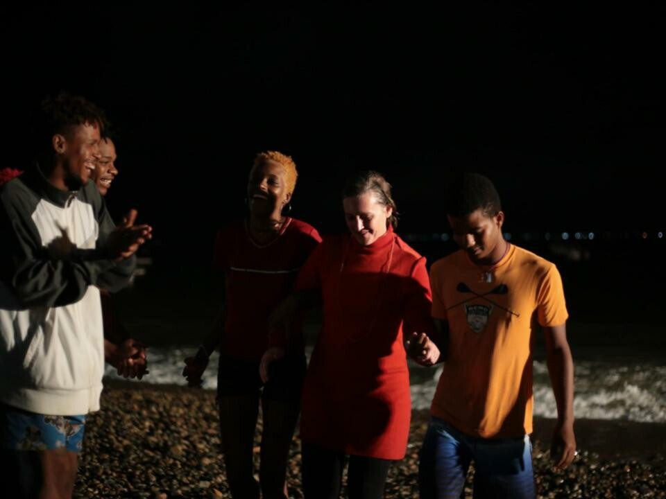 A few people dressed in red and orange near the ocean at night. 