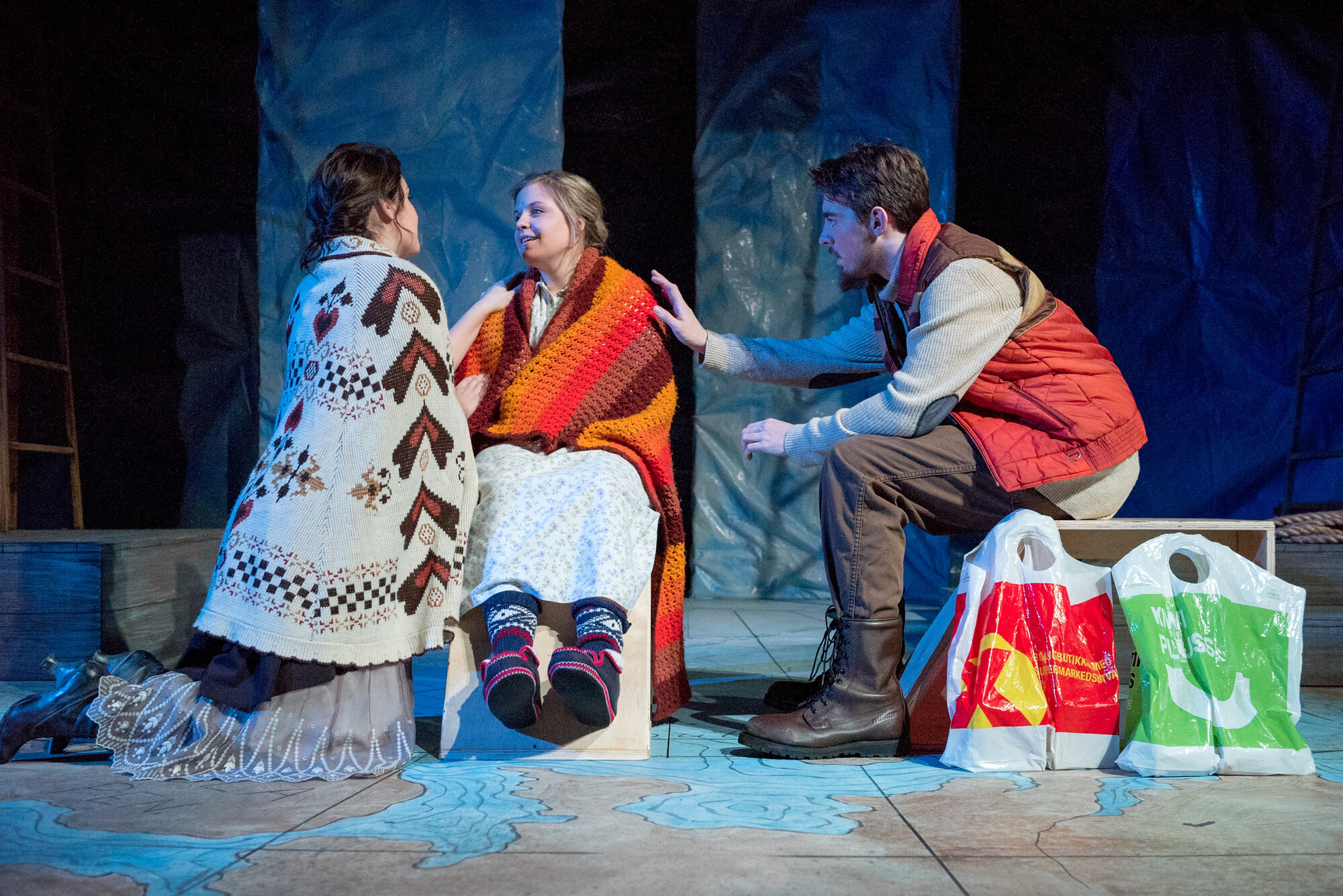 Three people in warn clothes sit around in a outdoor winter set. 