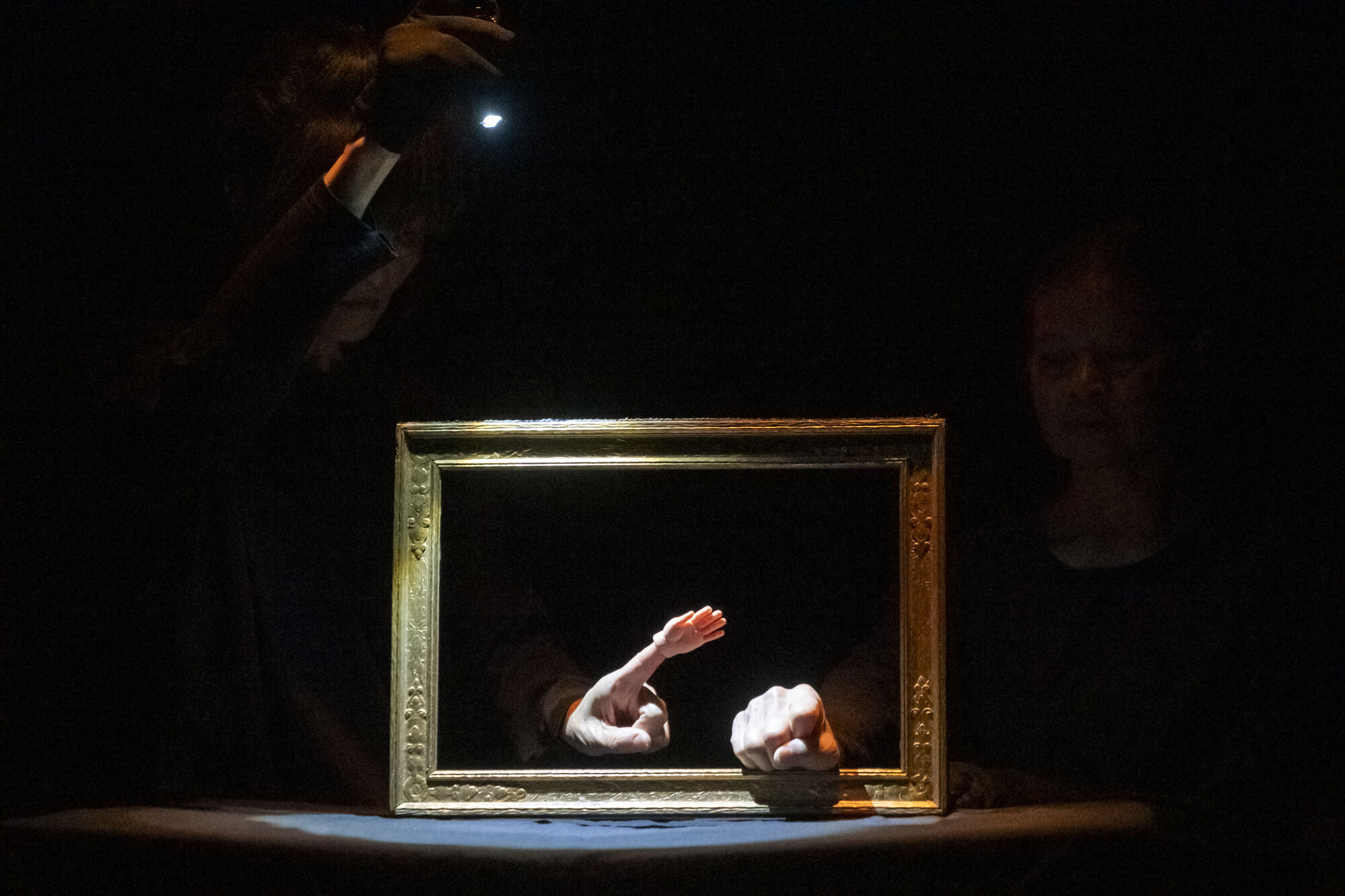 Two hands sticking out of a picture frame on a black background.