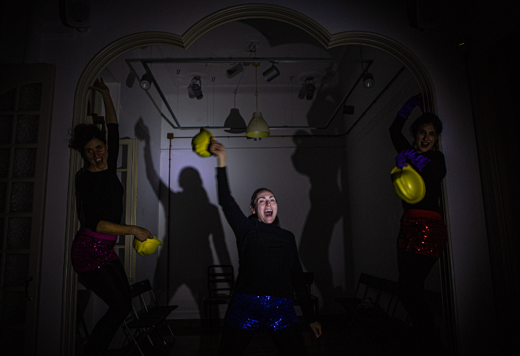 Three people in dark clothes in a dimly lit room throwing yellow construction hats in the hair.