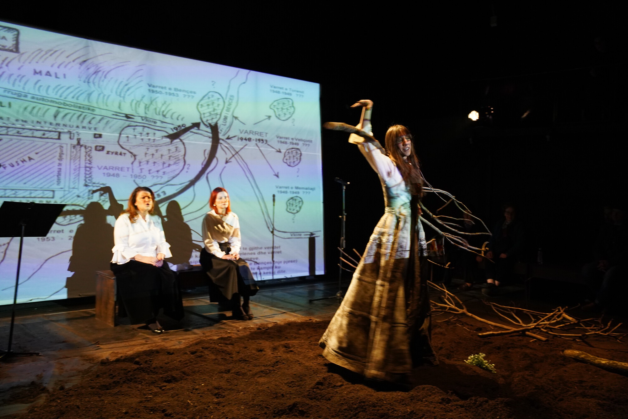 A person in a floor length dress with large tree limbs on stage.