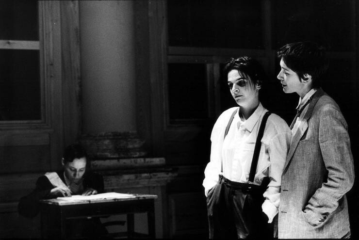A black and white photo of two people looking over someone writing on a desk.