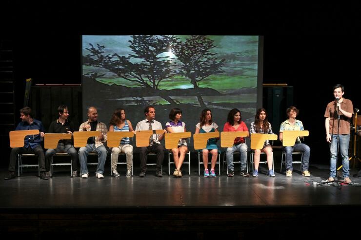 A group of people on stage sitting at a row of desks.