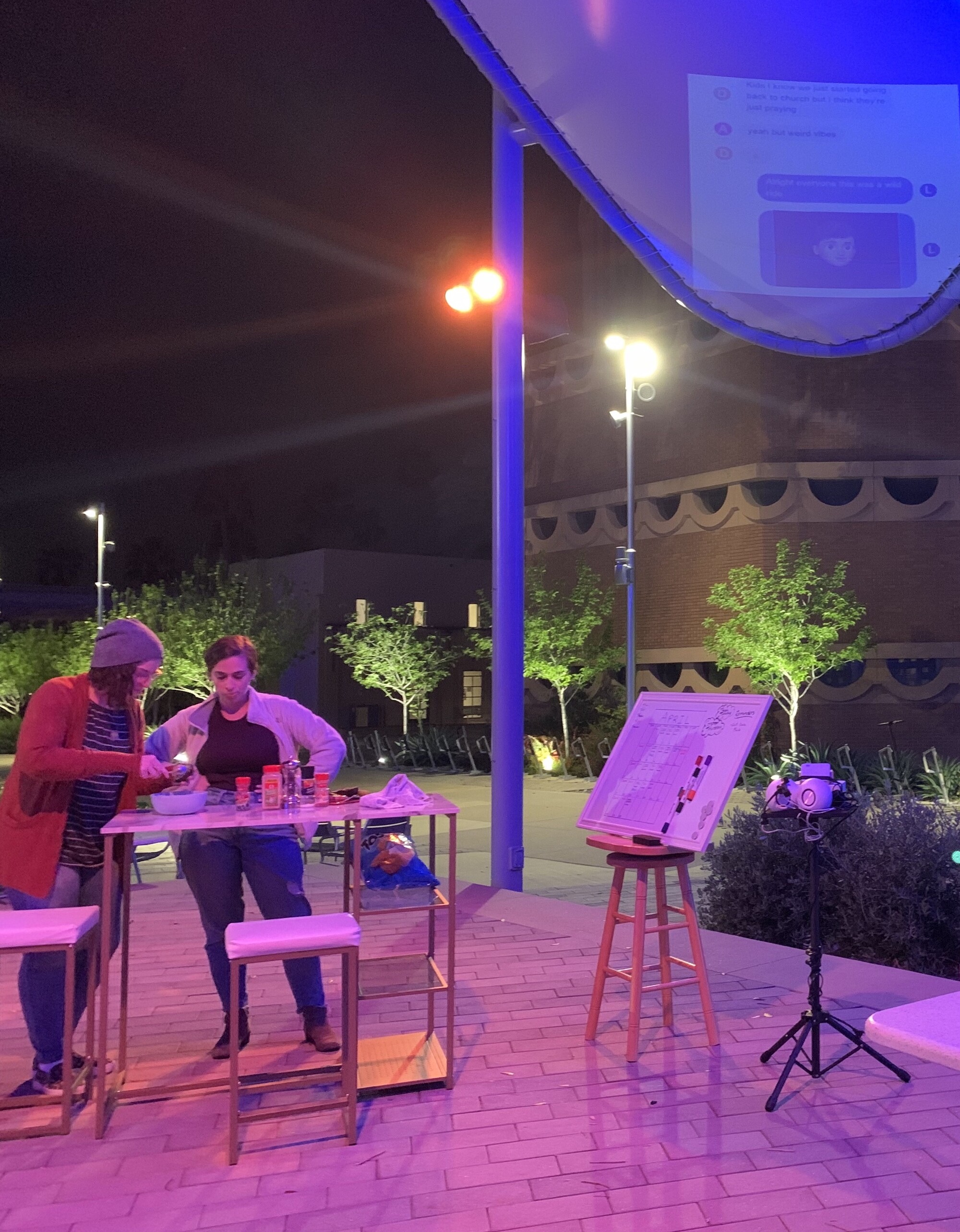 Two people and an easel outside in neon purple light.